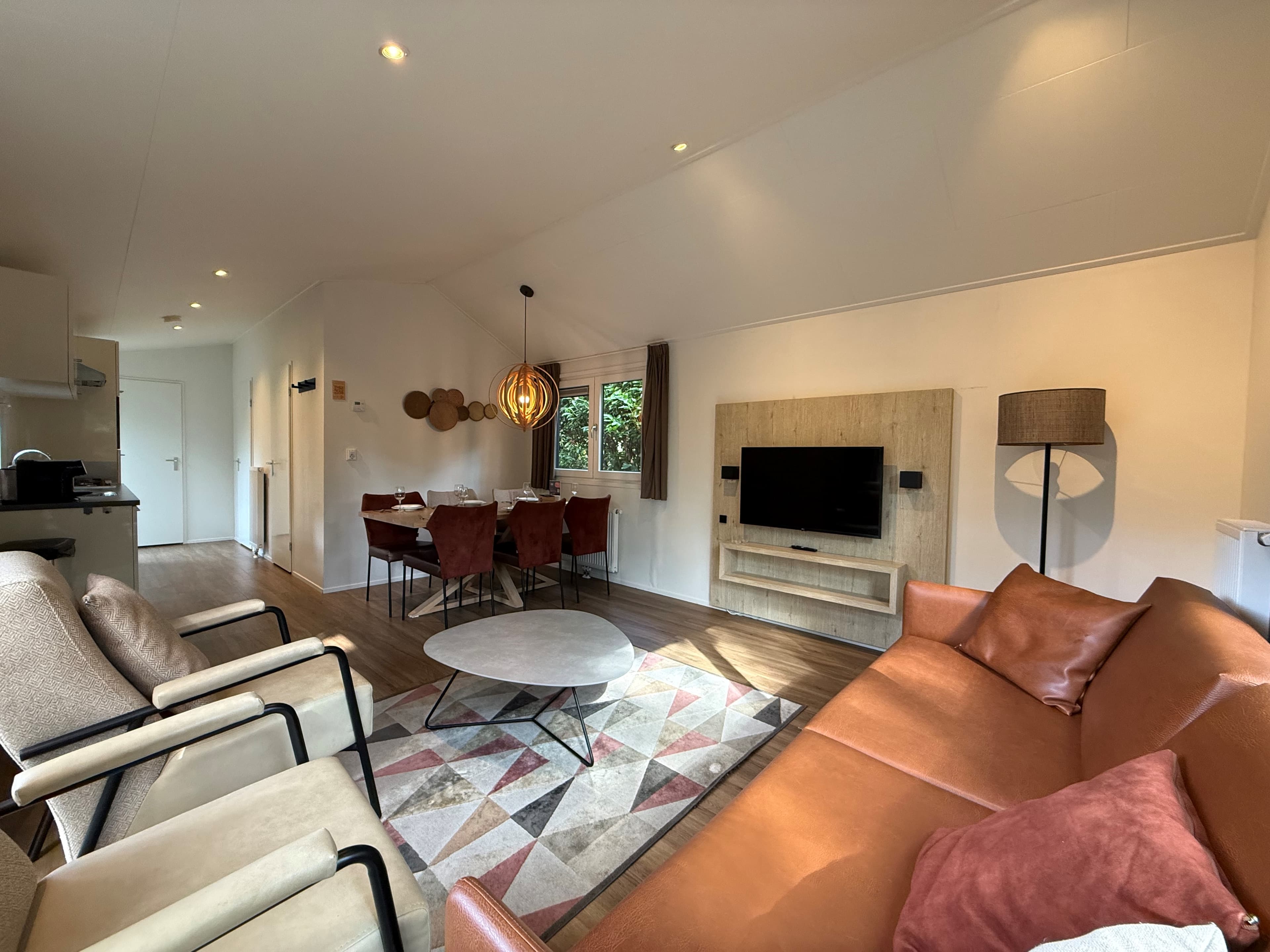 Moderne zithoek met een bank, stoelen, een eettafel en een tv, lichte inrichting met raam voor natuurlijk licht.