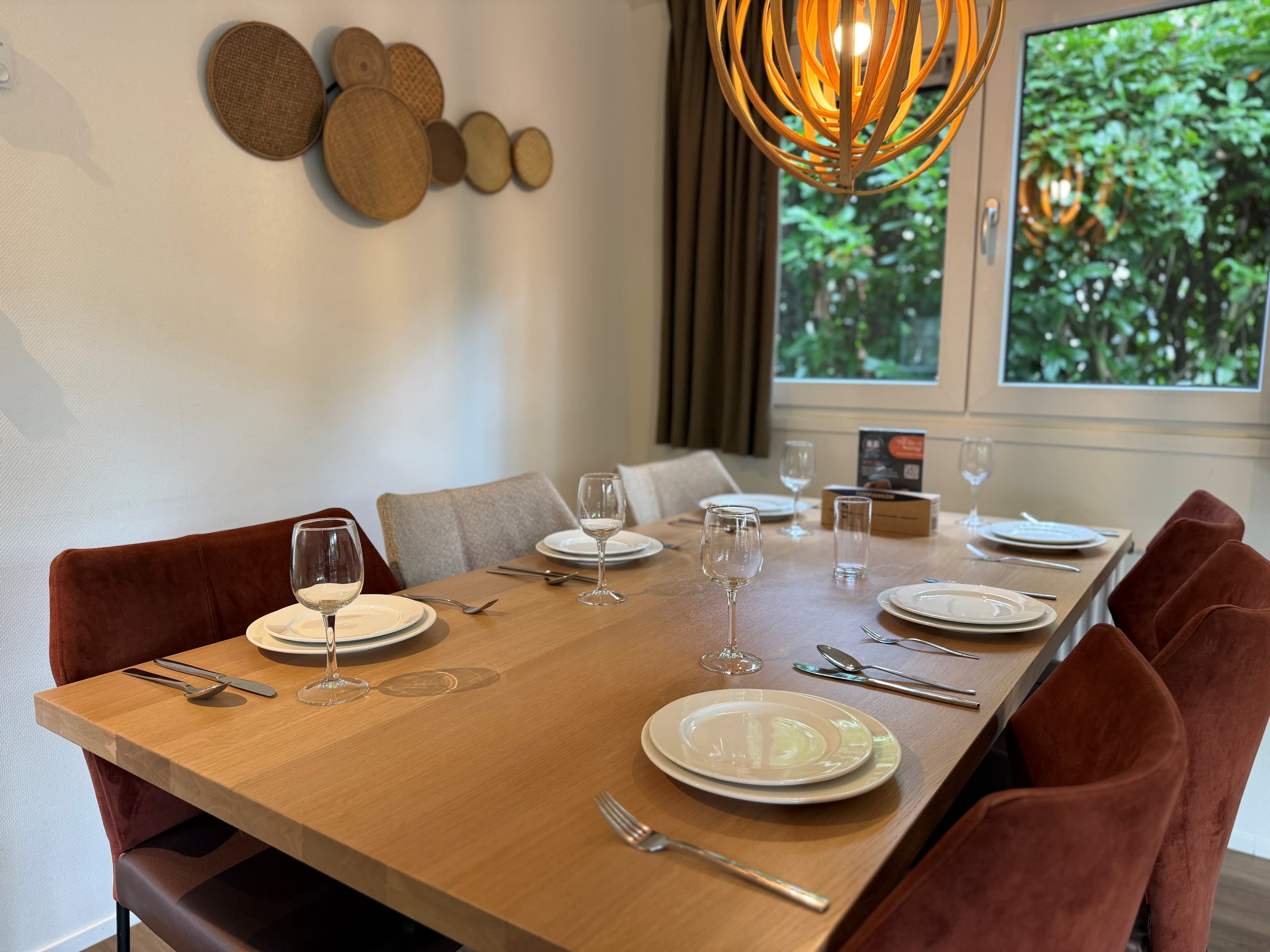 Eetkamer met grote houten tafel, acht stoelen, borden en glazen, en muurdecoratie met houten schalen.