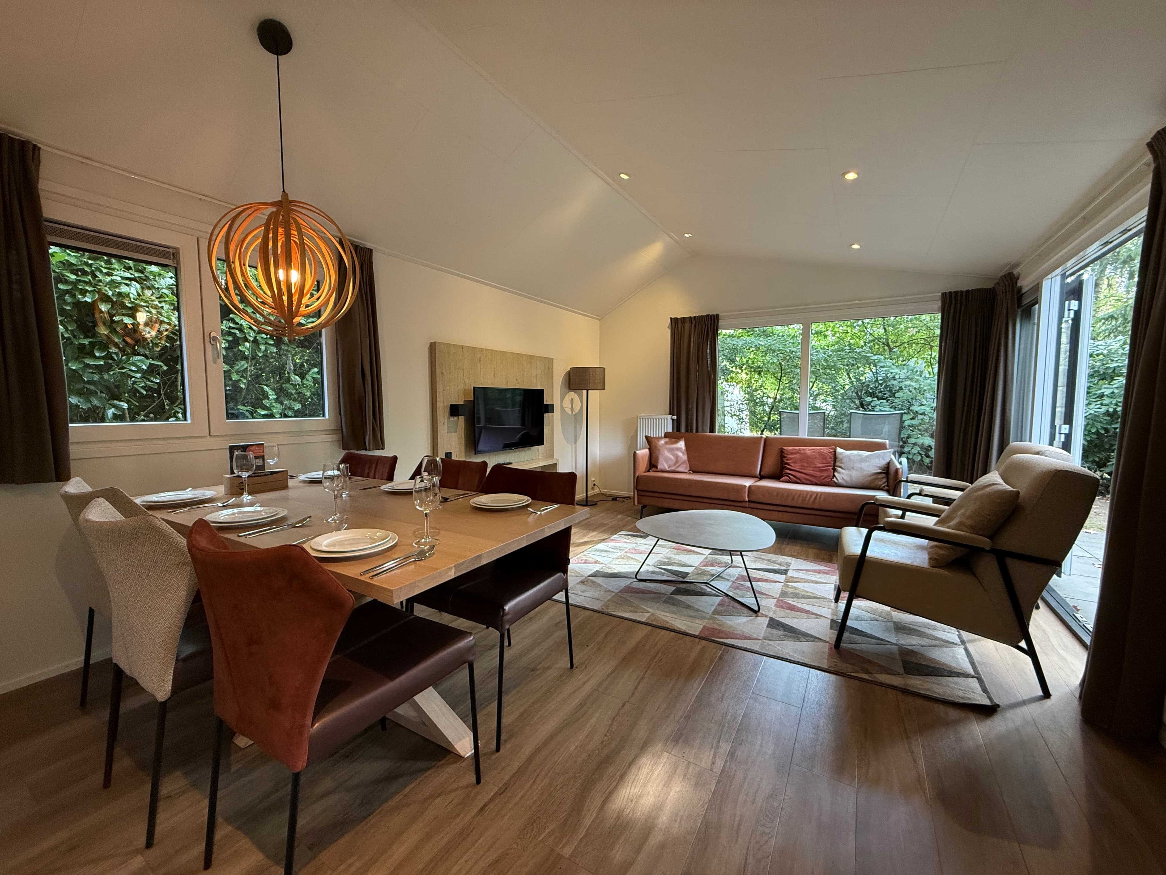 Moderne woonkamer met eettafel, zithoek, grote ramen en toegang tot een buitenruimte met groen uitzicht.