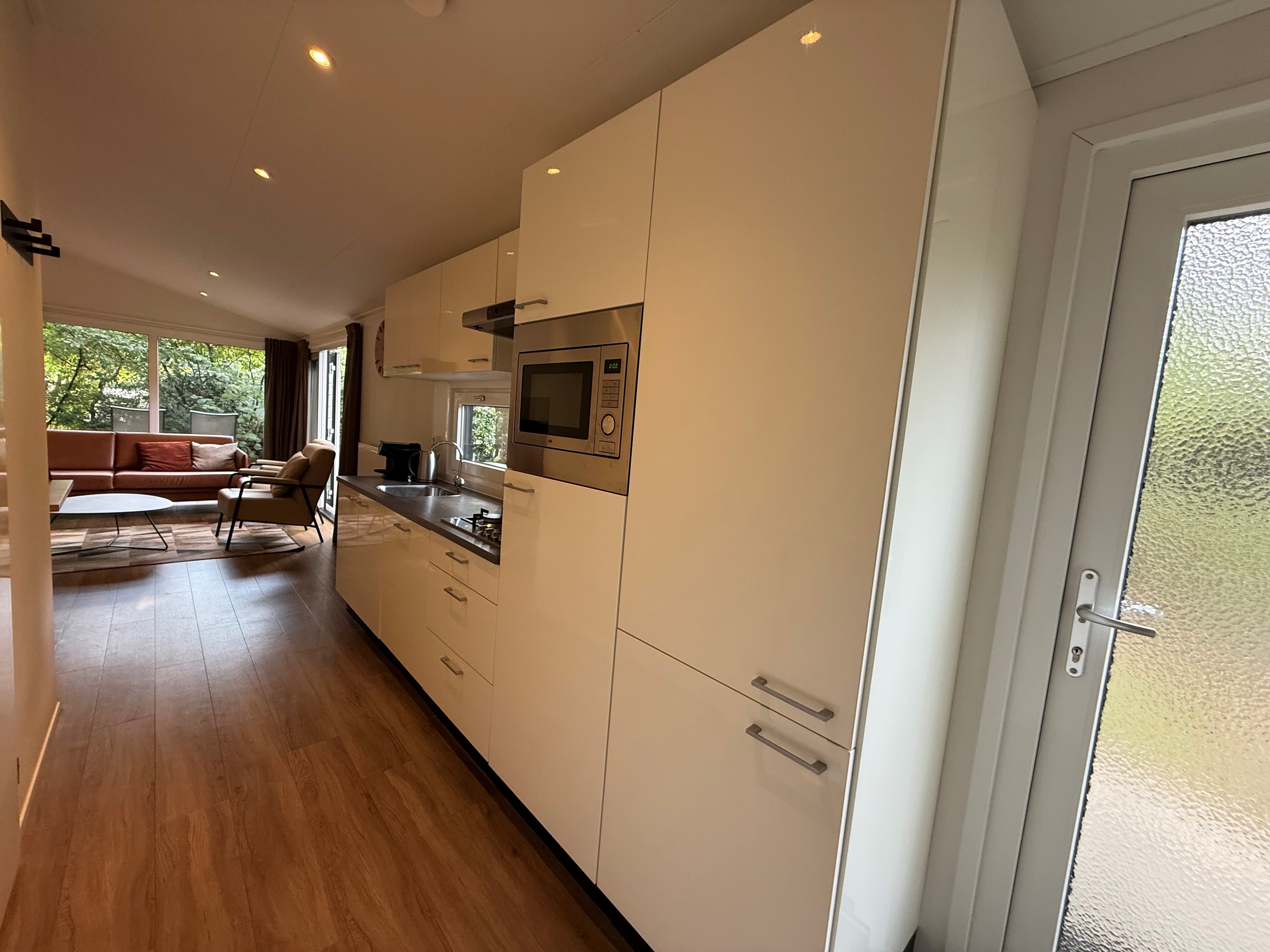 Moderne keuken met ingebouwde apparatuur en toegang tot de woonkamer met grote ramen en zithoek.