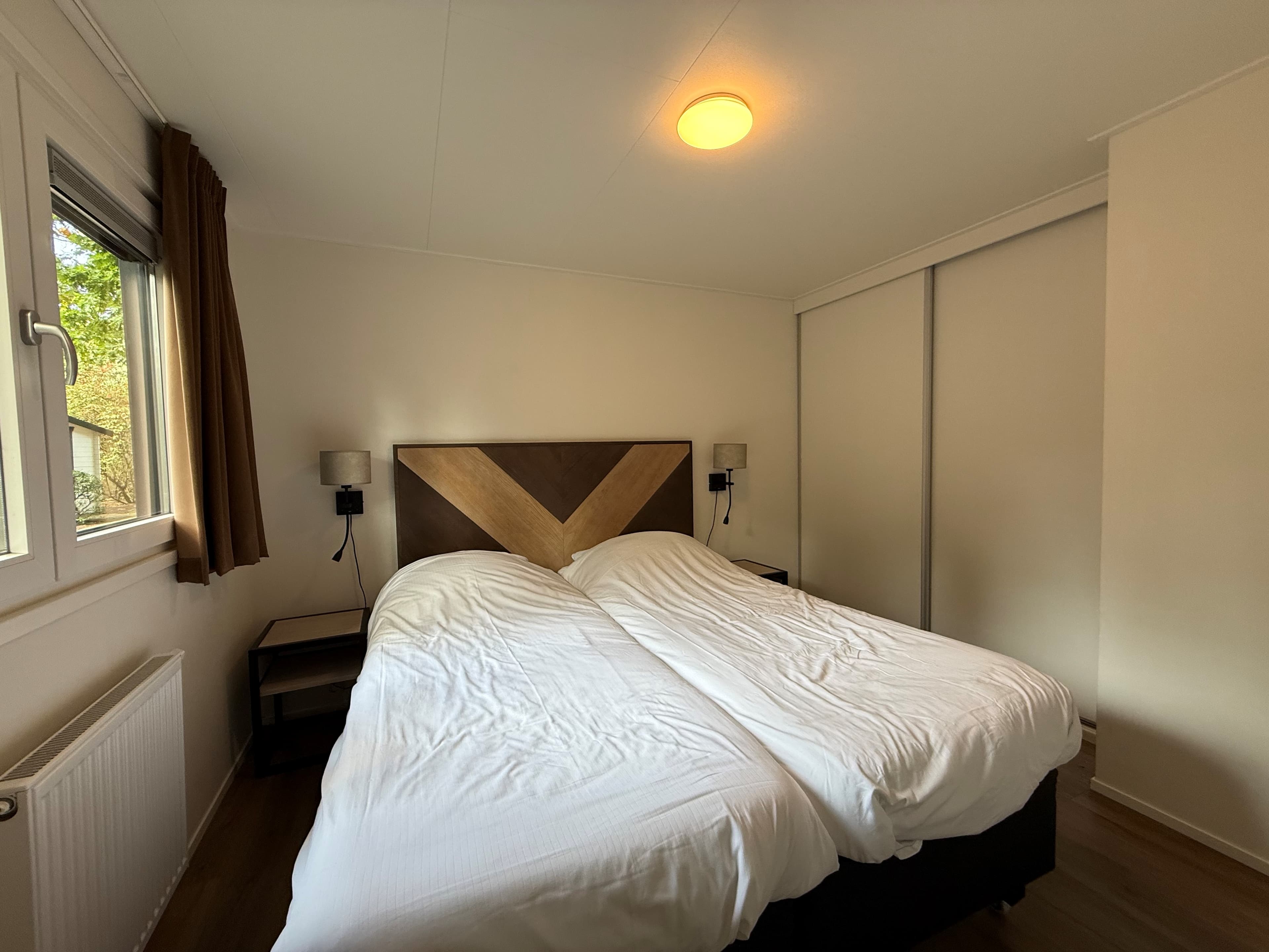 Slaapkamer met twee aansluitende bedden, nachtkastjes, raam met gordijnen en inbouwkast tegen de wand