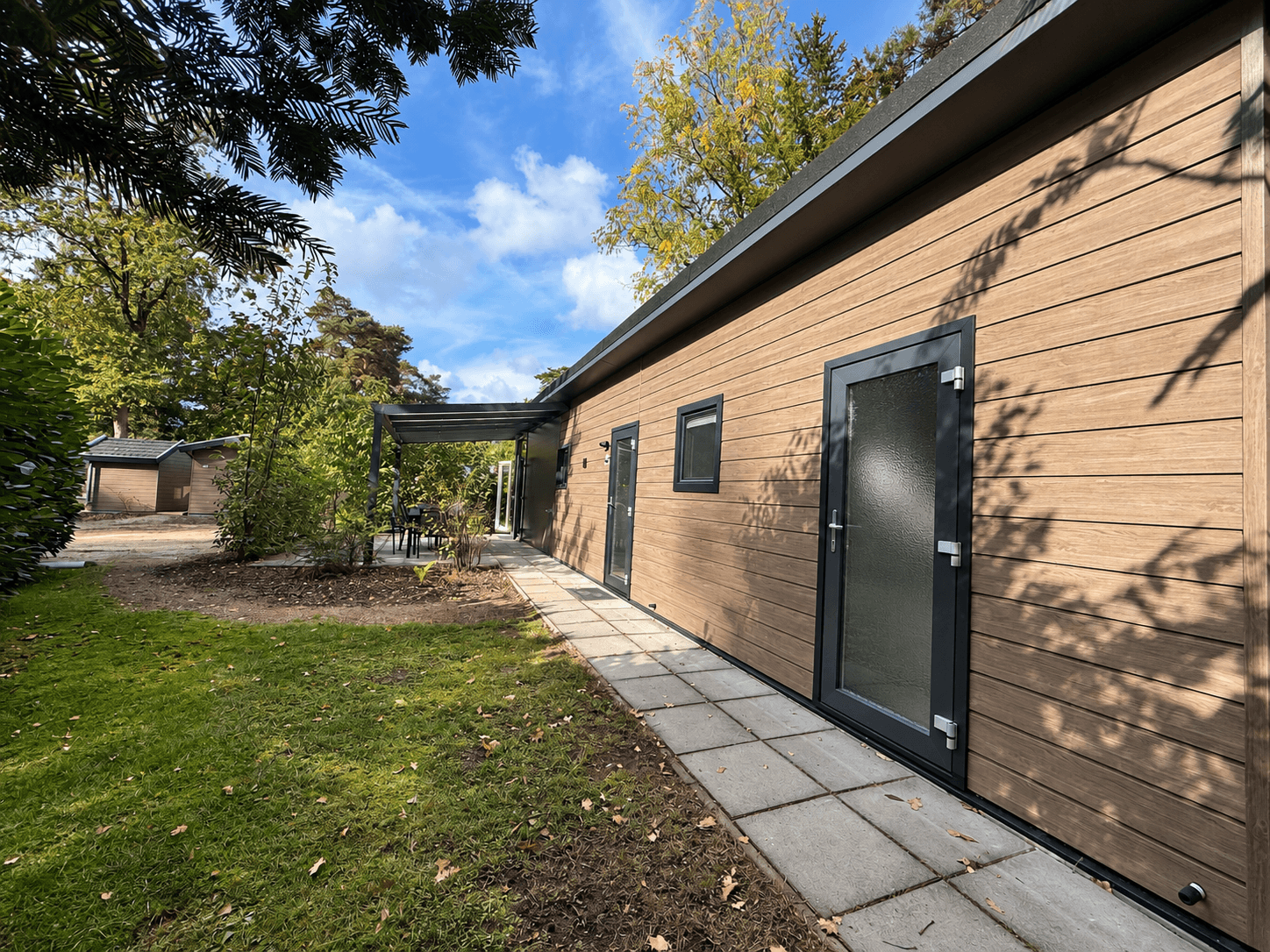Moderne recreatiewoning met houten gevel, betegeld pad en groene omgeving op Veluwepark de Bosgraaf, Lieren