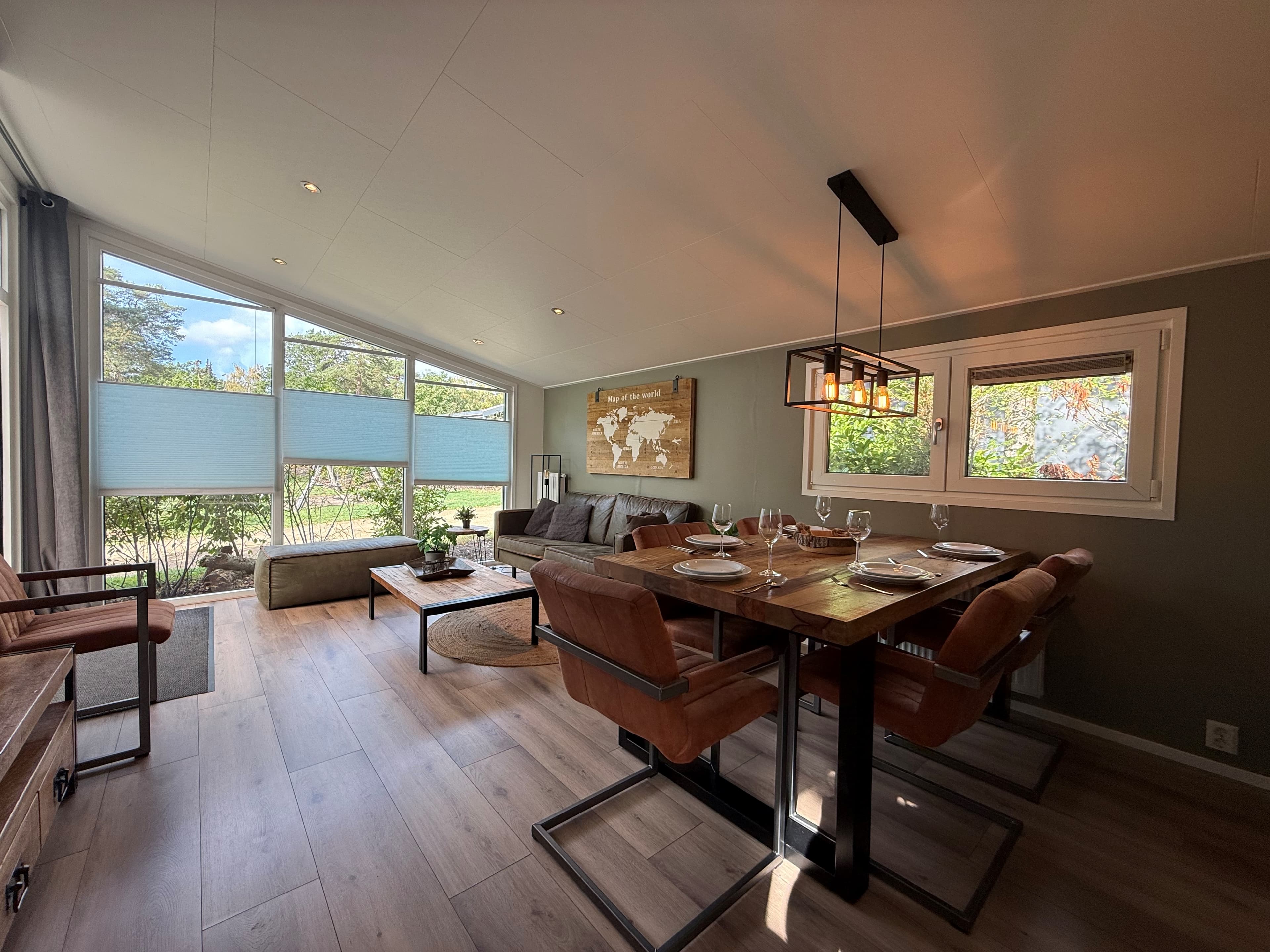 Gezellige woonkamer met eettafel, comfortabele bank en grote ramen met uitzicht op de tuin