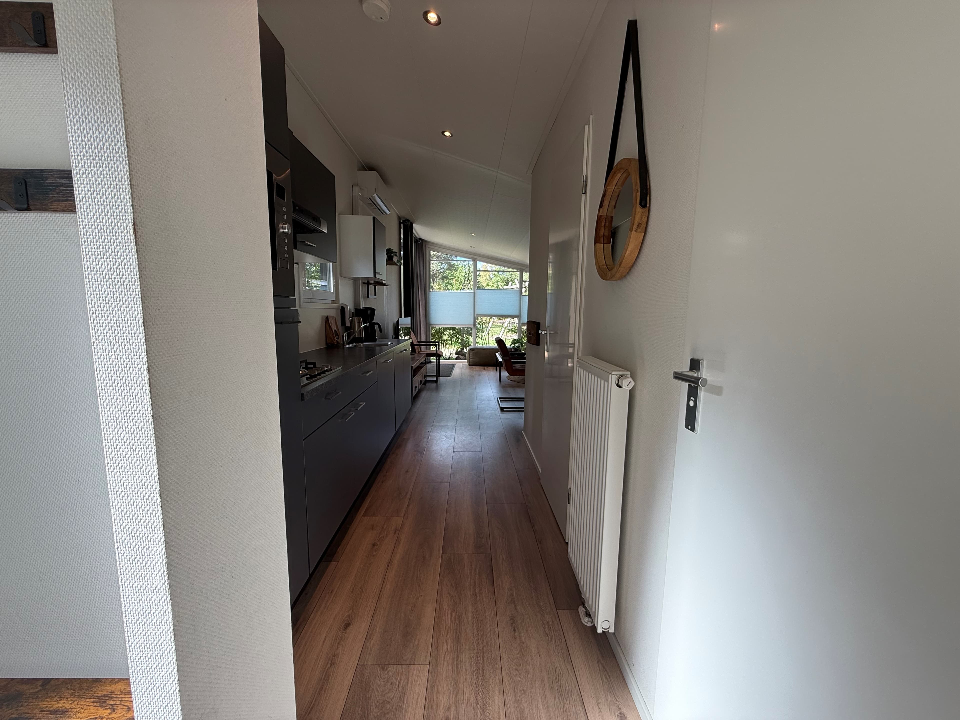 Moderne keuken met toegang tot een lichte woonkamer met grote ramen en natuurzicht, lange gang met laminaatvloer