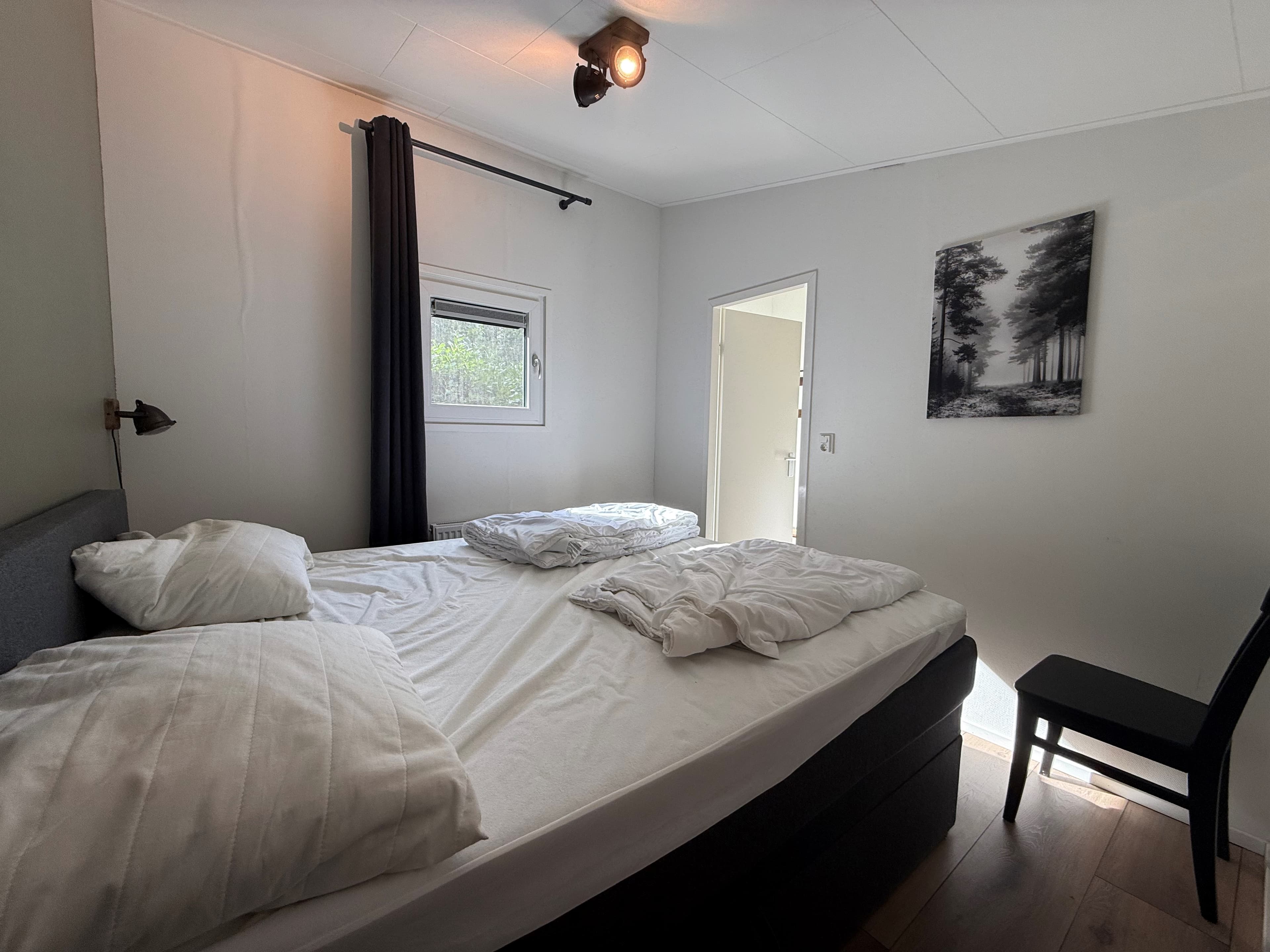 Slaapkamer met twee eenpersoonsbedden, raam met uitzicht en een zwarte stoel in de hoek.
