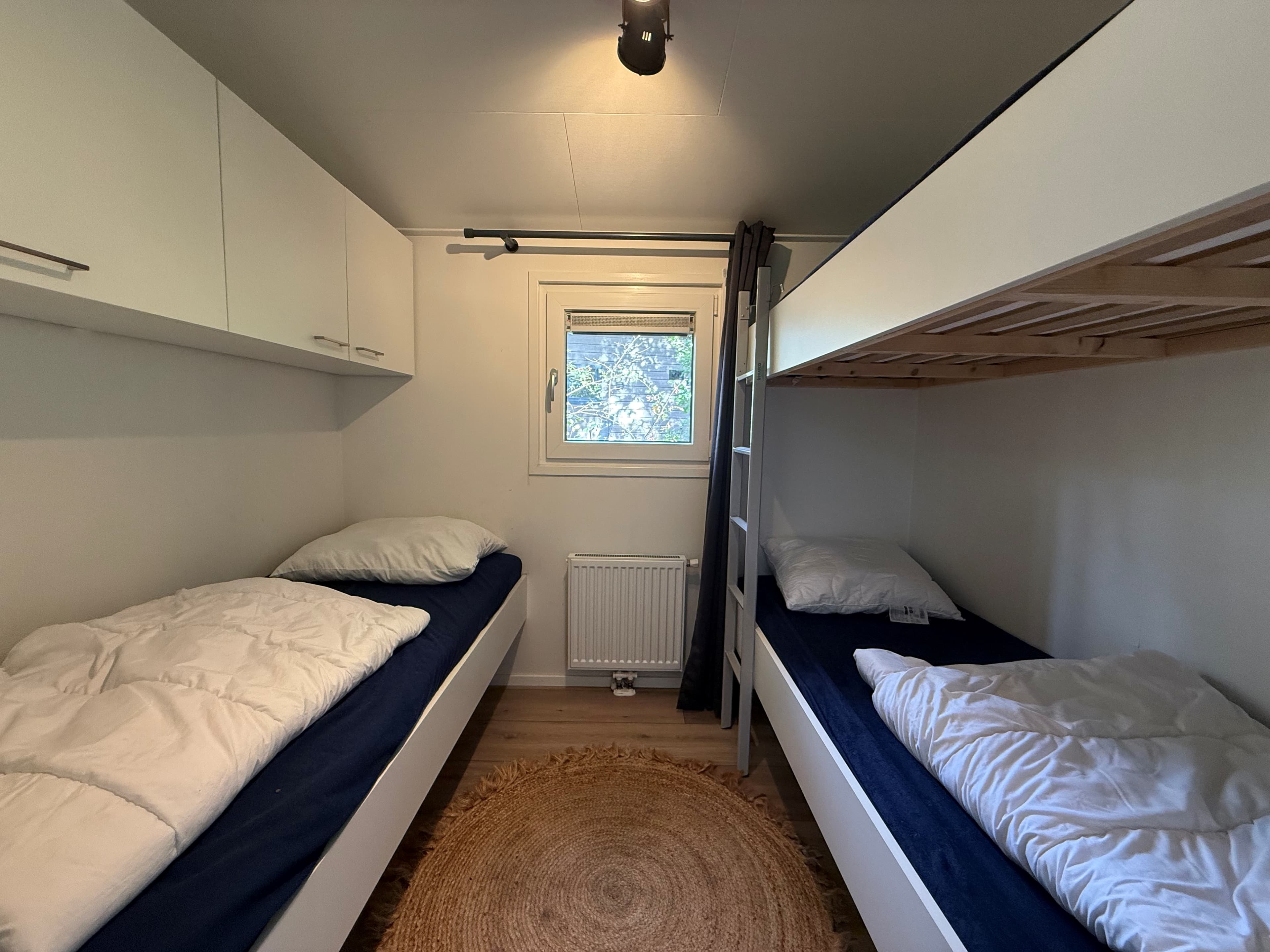 Slaapkamer met twee eenpersoonsbedden, wandkast en een raam met zicht op bomen, op een houten vloer met een rond vloerkleed