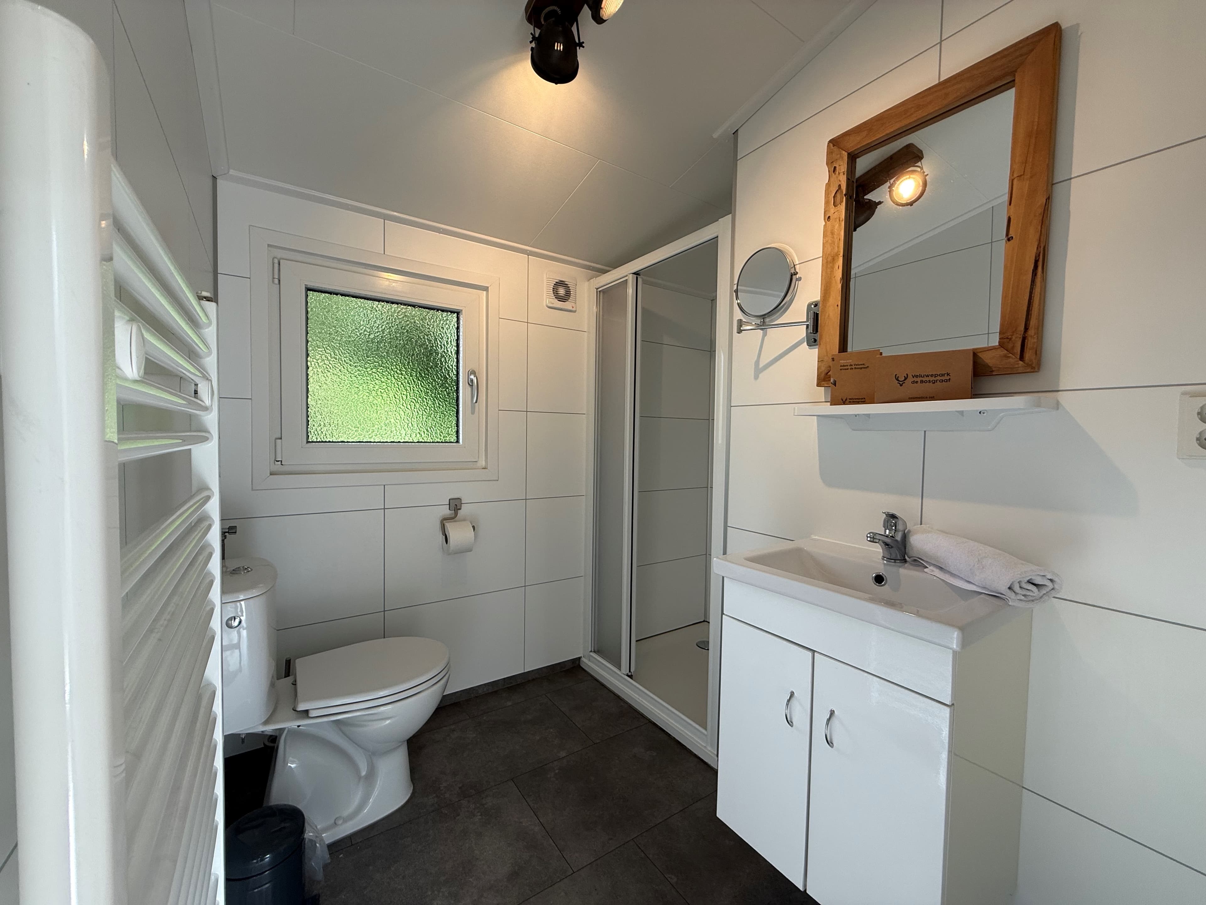 Moderne badkamer met douche, wastafel, toilet en spiegel, heldere muren en tegelvloer
