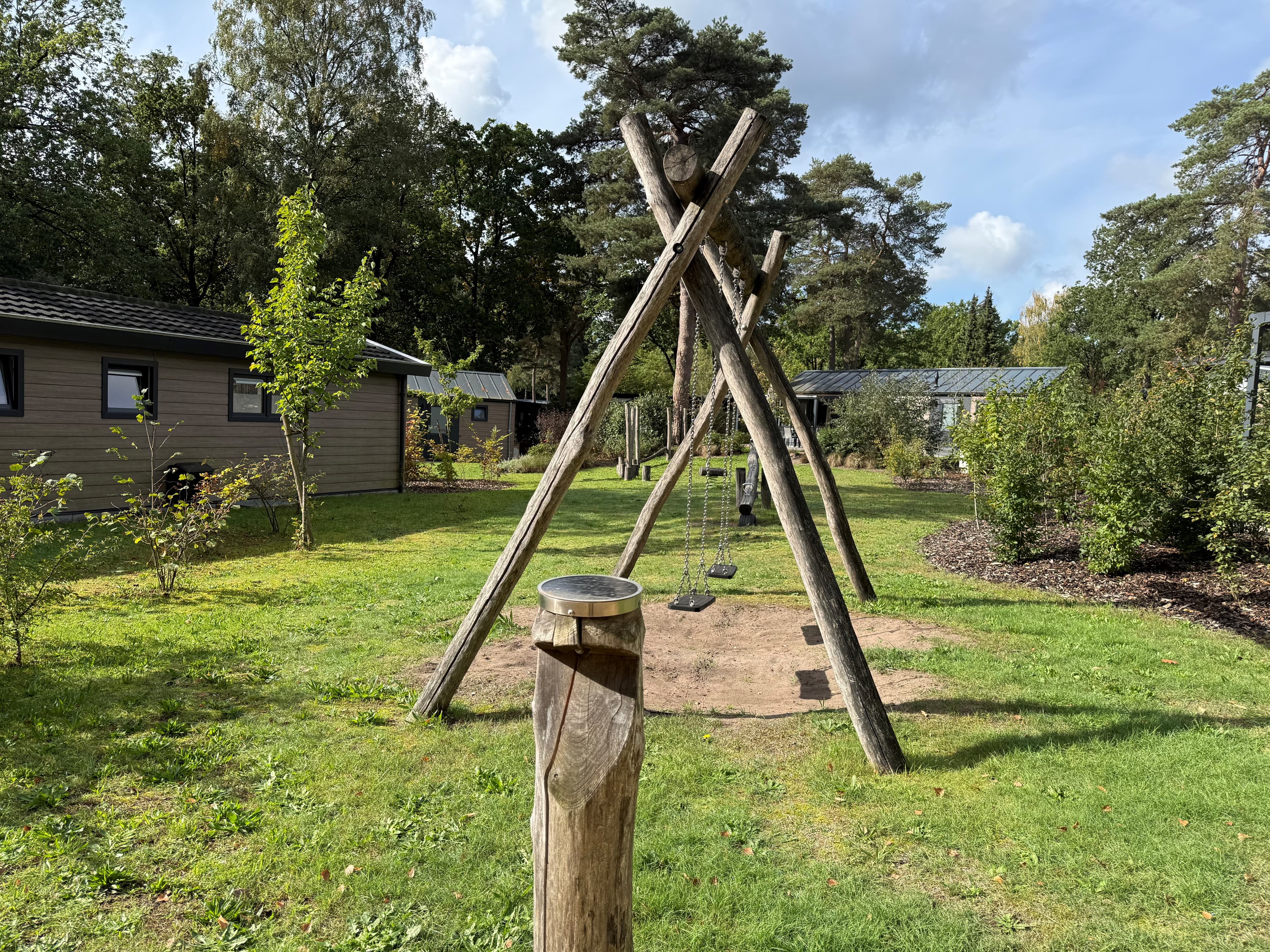 Speeltuin met houten schommel en zandbed, omringd door groen en vakantiewoningen in Veluwepark de Bosgraaf