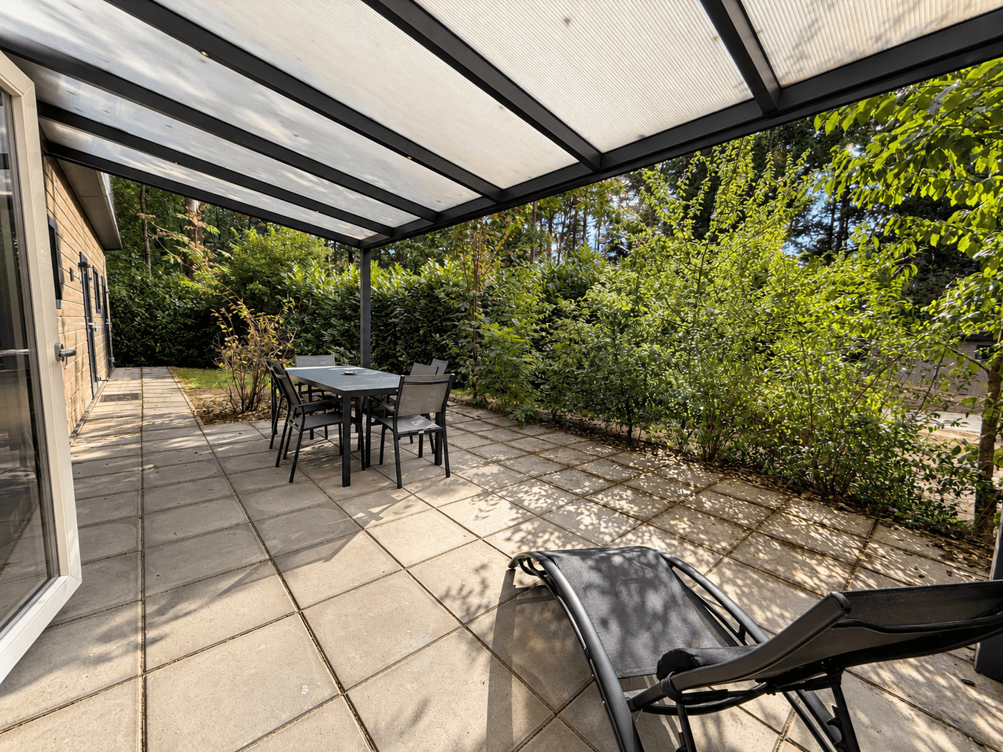 Terras met tegelvloer, meubels en parasol omringd door groen in Recreatiewoning op Veluwepark de Bosgraaf te Lieren
