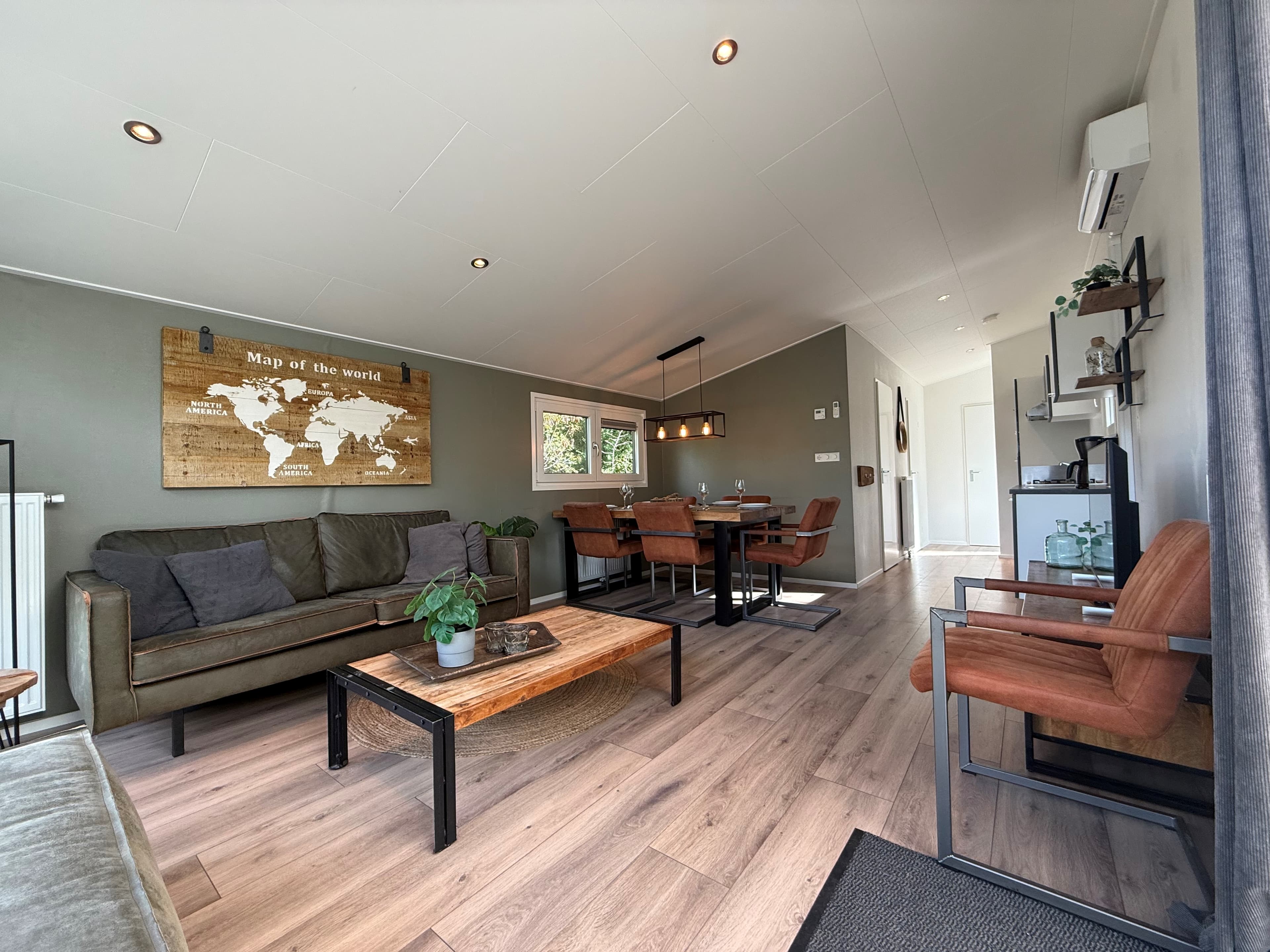 Woonkamer met bank, houten tafel en stoelen, grote ramen en sfeervolle wanddecoratie van een wereldkaart