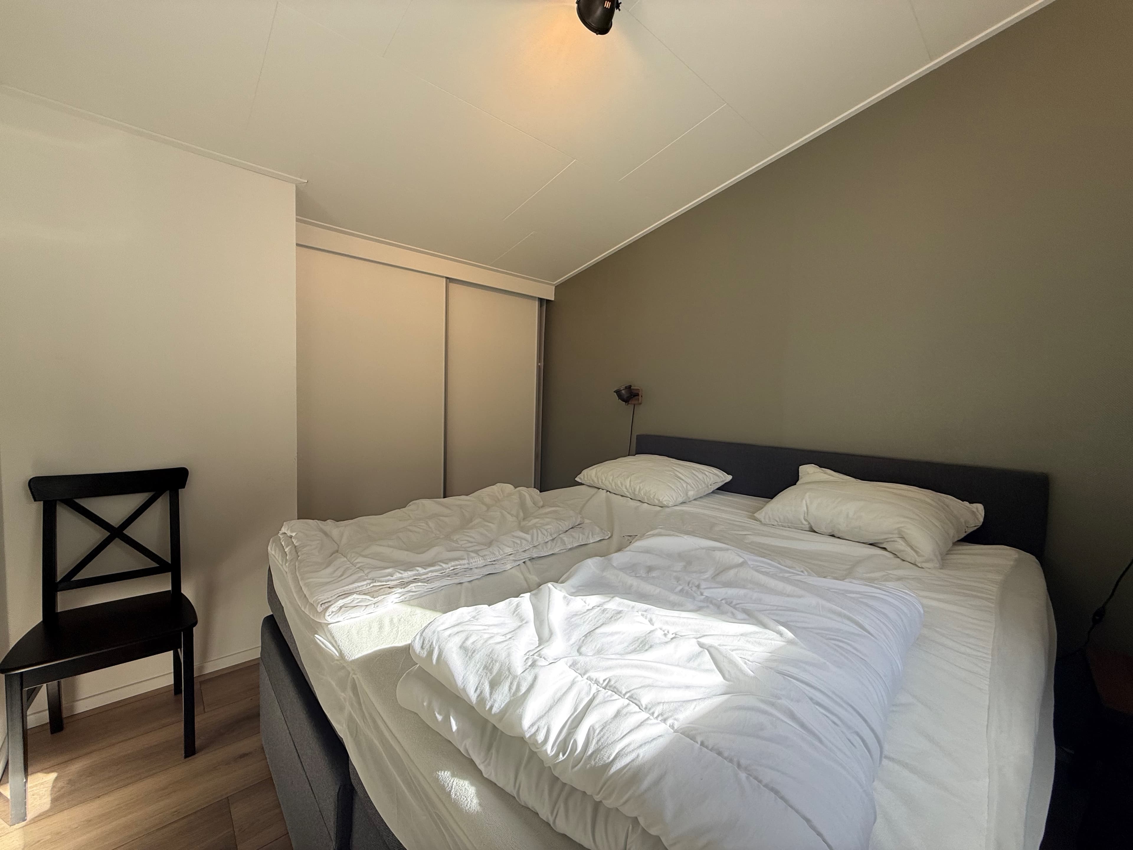 Slaapkamer met twee eenpersoonsbedden, een stoel en een wand met een neutrale kleur.