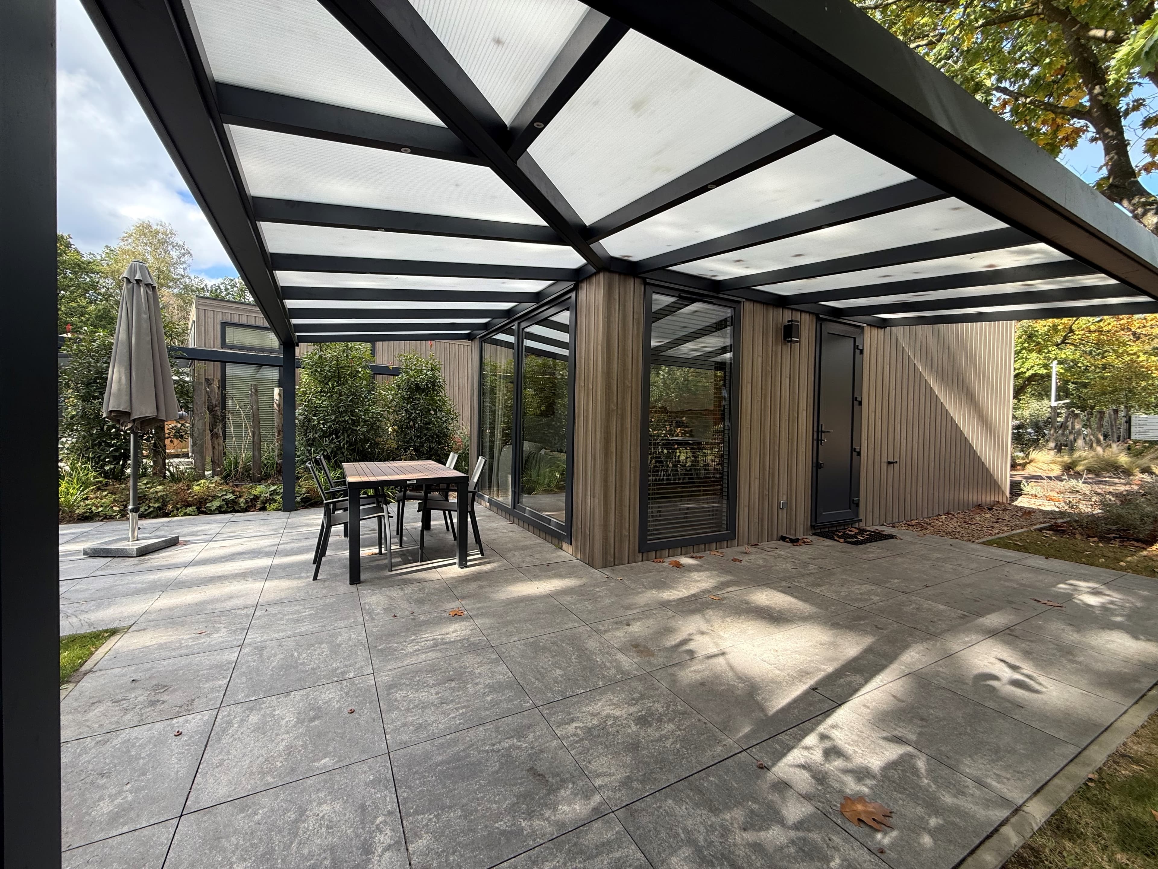 Moderne recreatiewoning met overdekt terras, houten gevel en een betegelde patio omgeven door groen natuur.