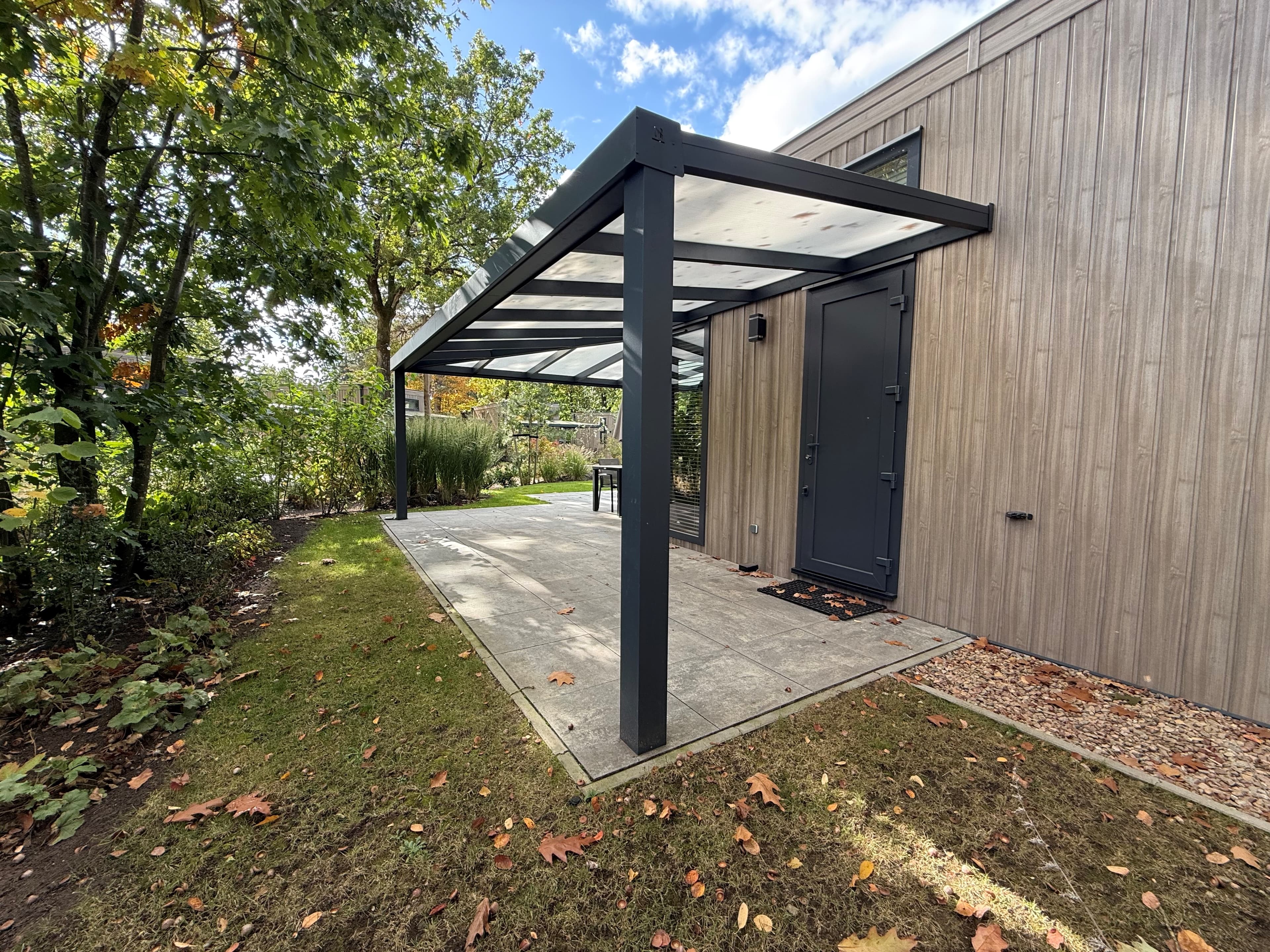 Overdekte patio aan de zijkant van de bungalow met een tegelvloer en groene beplanting rondom.