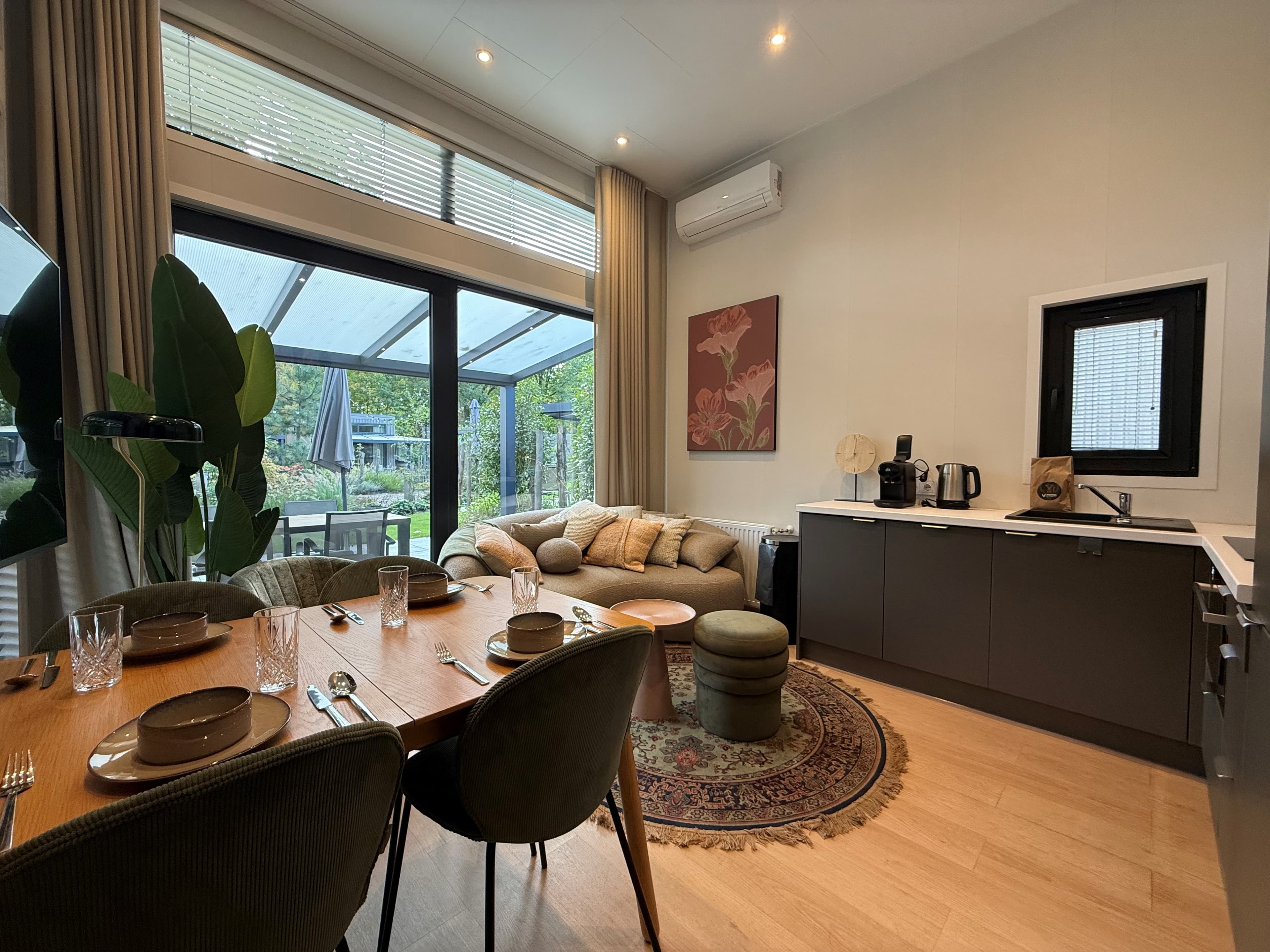 Moderne eet- en woonruimte met grote ramen, een houten tafel, comfortabele stoelen en een open keuken met apparatuur