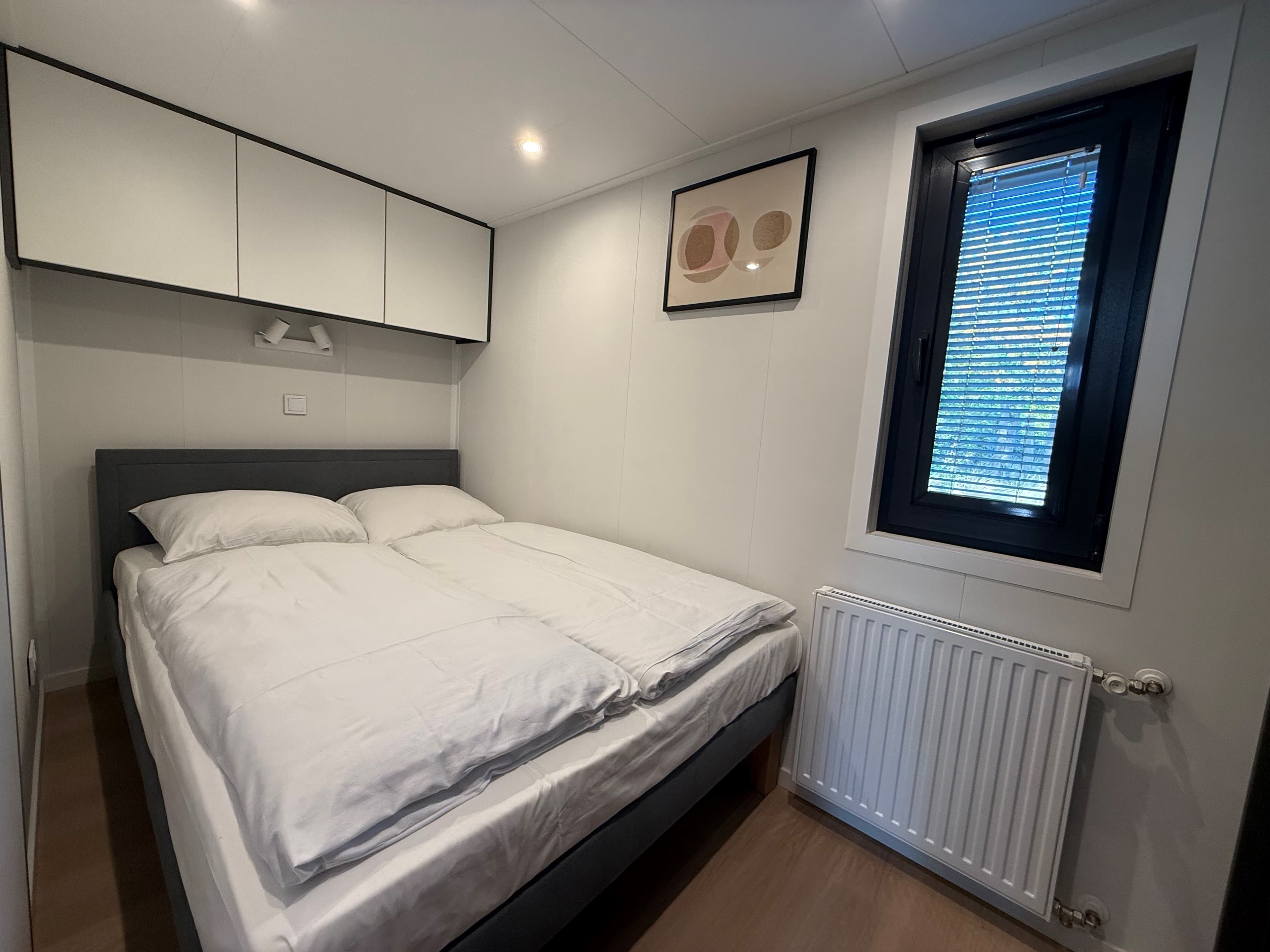 Slaapkamer met een tweepersoonsbed, modern meubel en een raam met jaloezieën.