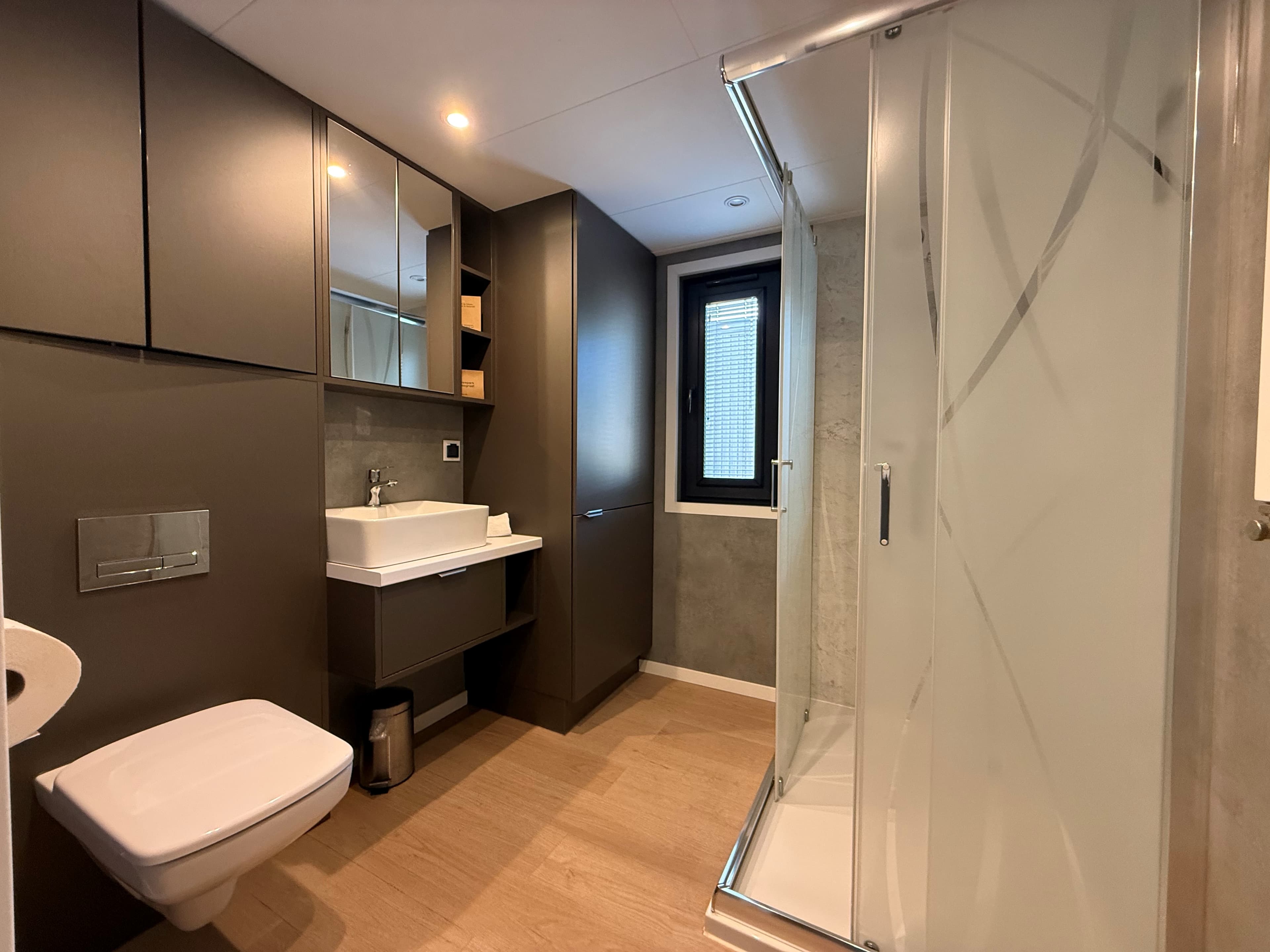 Moderne badkamer met douche, wastafel, spiegelkasten en toilet in neutrale kleuren.