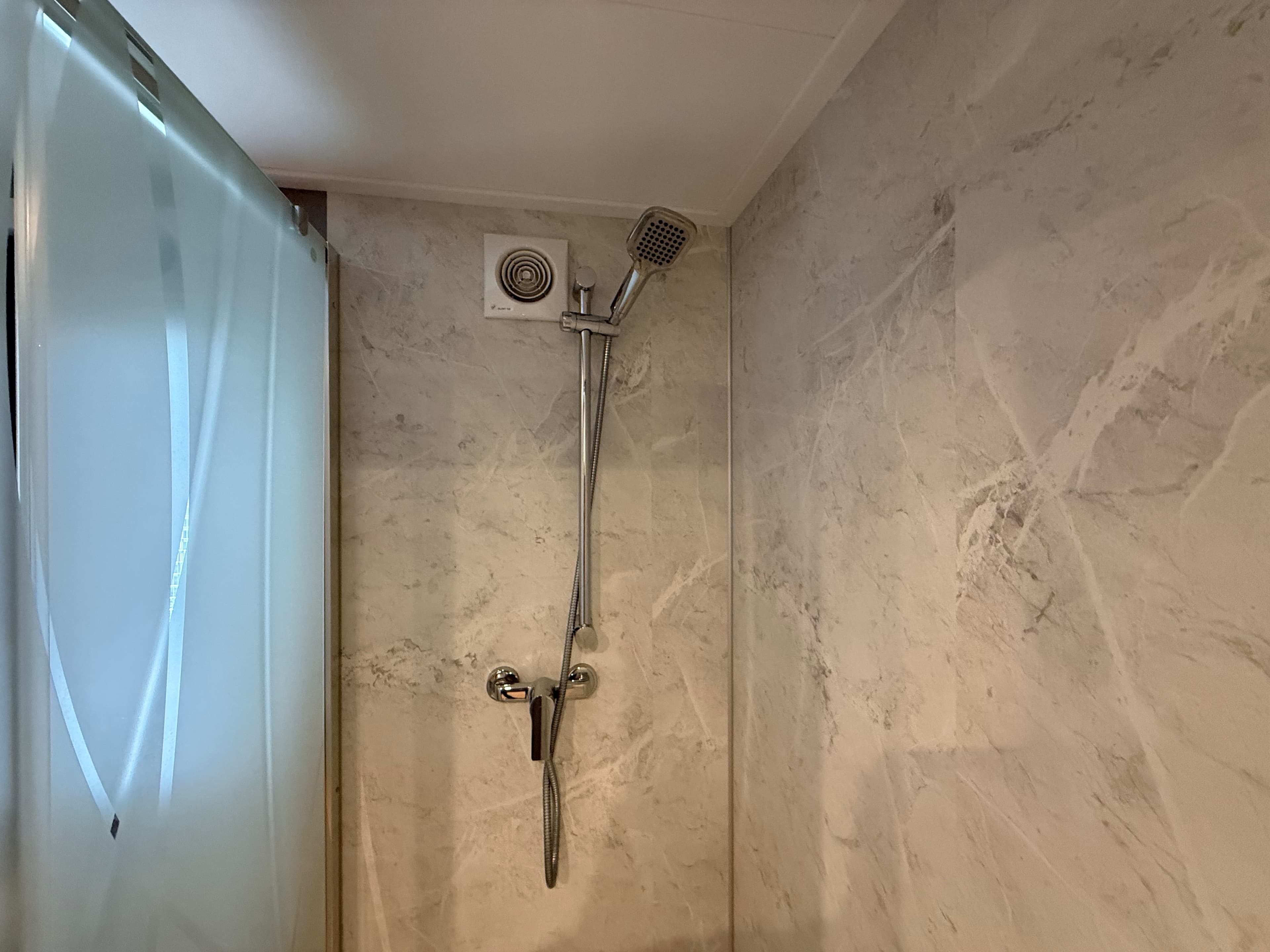 Douche met moderne kranen en een marmerachtig tegelmotief in een recreatiewoning.