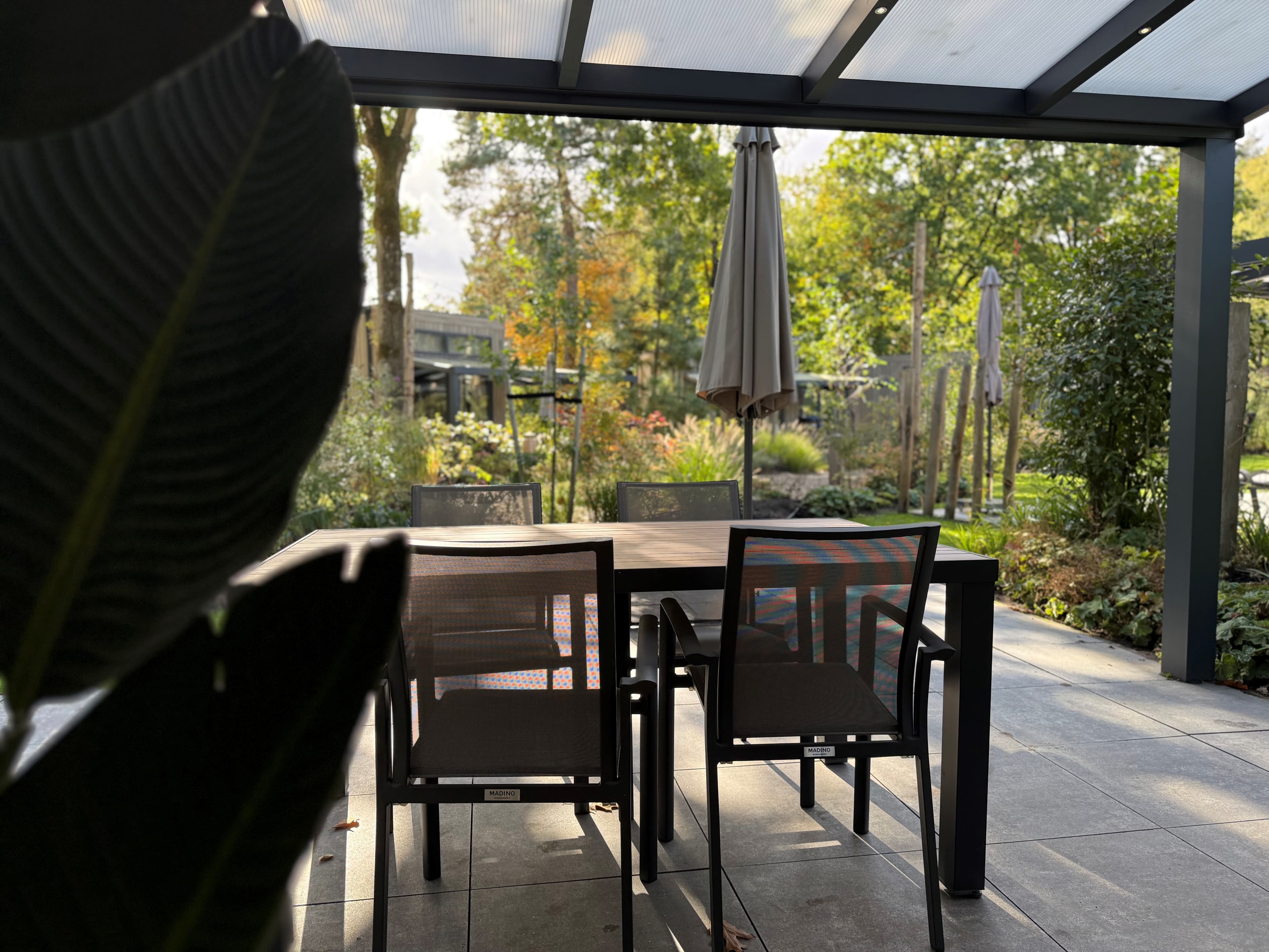 Terras met een tafel en stoelen, omringd door groen en bomen, met een parasol op de achtergrond.