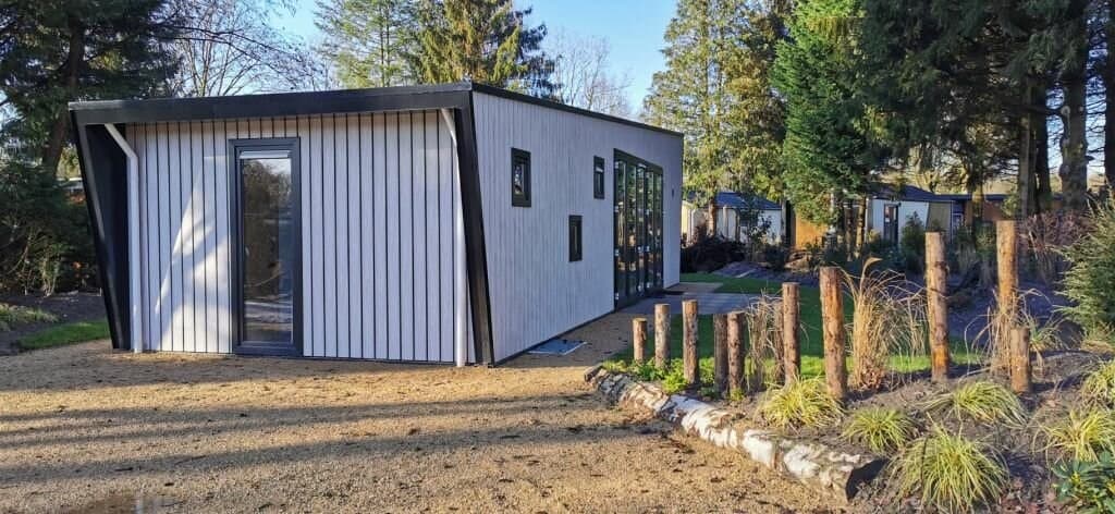 Moderne vakantiehuis met een houten gevel, grote ramen en een groene omgeving met tuinafscheiding van takken.