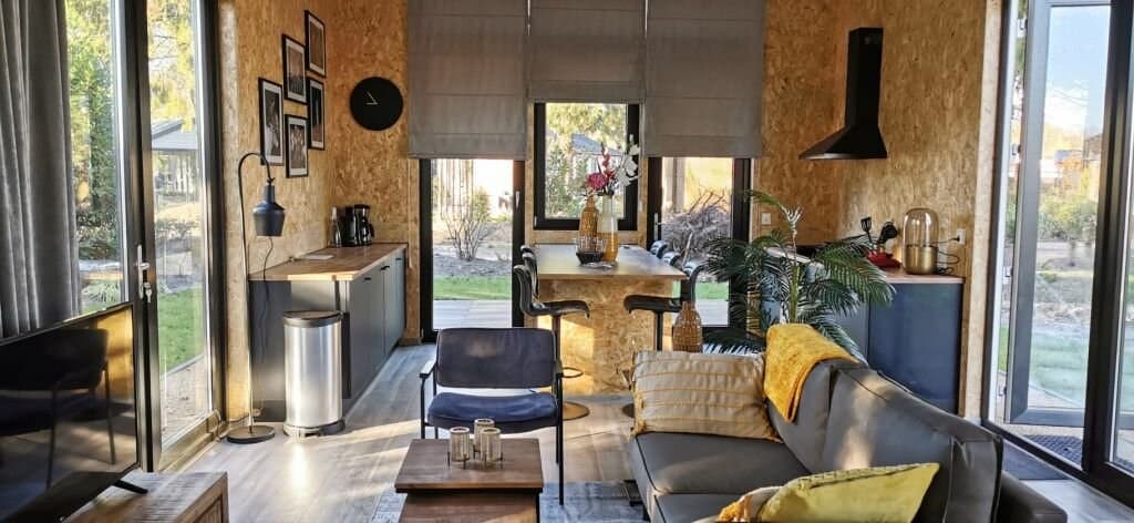 Moderne woonkamer met grote ramen, eettafel, bank en een open keuken met planten en natuurlijke materialen