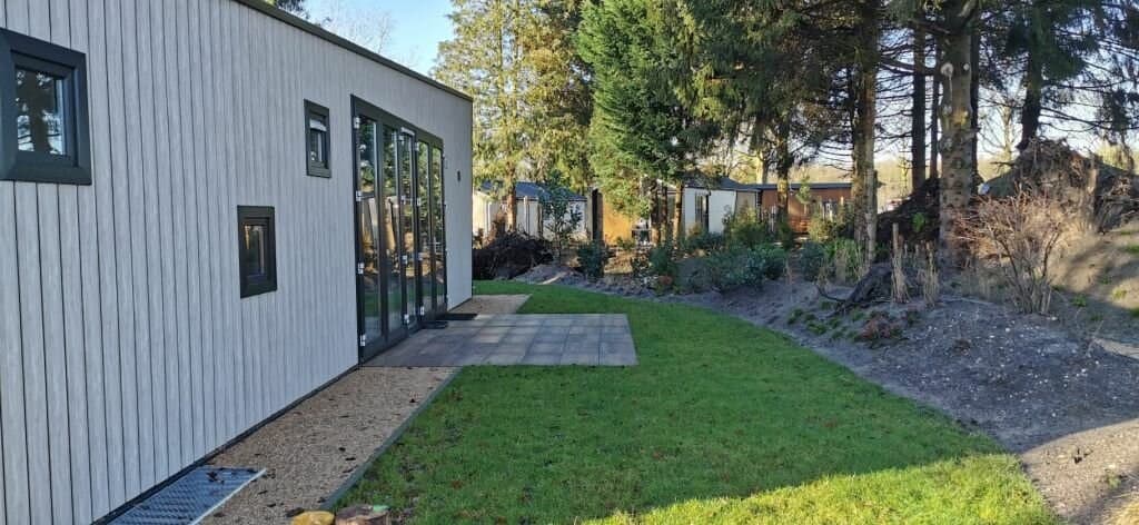 Moderne woning met grote ramen, terras van tegels en grasland met groene begroeiing rondom