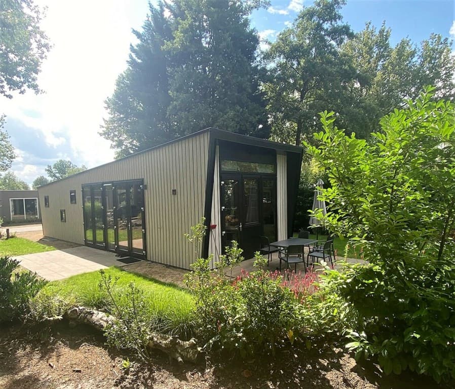 Moderne vakantiewoning met grote ramen, een terras en groene beplanting rondom, gelegen in een rustige omgeving