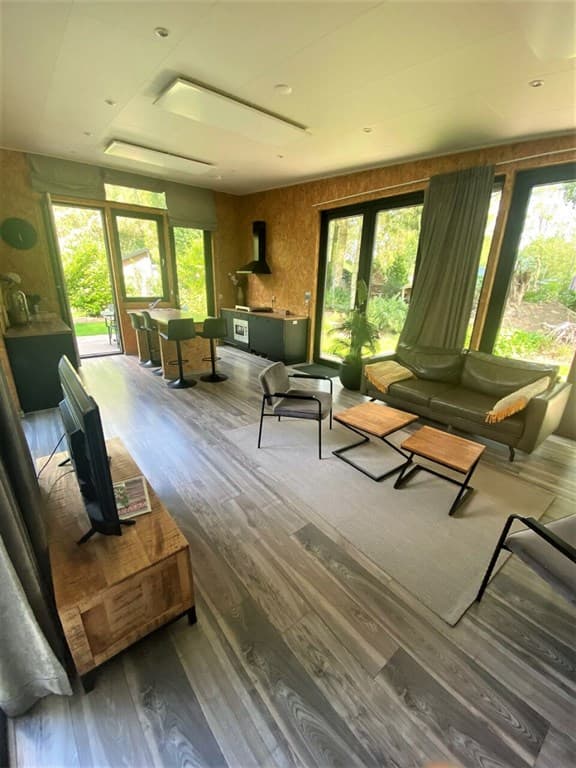 Zithoek met banken en tafel, grote ramen met uitzicht op de tuin, eettafel met stoelen en moderne inrichting.