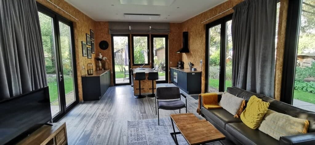 Woonkamer met grote ramen, moderne meubels, een eetgedeelte en toegang tot de tuin