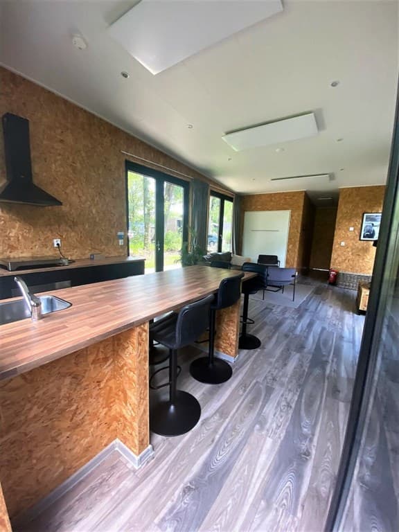 Moderne keuken met houten werkblad, barstools en grote ramen met uitzicht op de natuur.