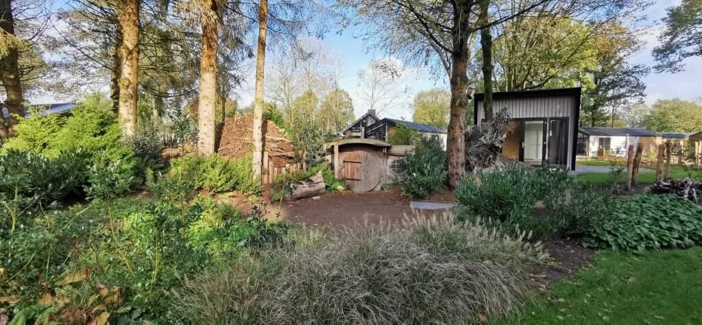 Groene tuin met bomen en struiken, houten elementen en een moderne woning op de achtergrond in EuroParcs Zuiderzee.
