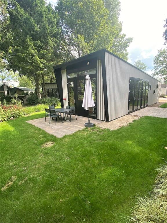 Moderne vakantiewoning met groot terras, tuinmeubelen en een parasol, omringd door groen.