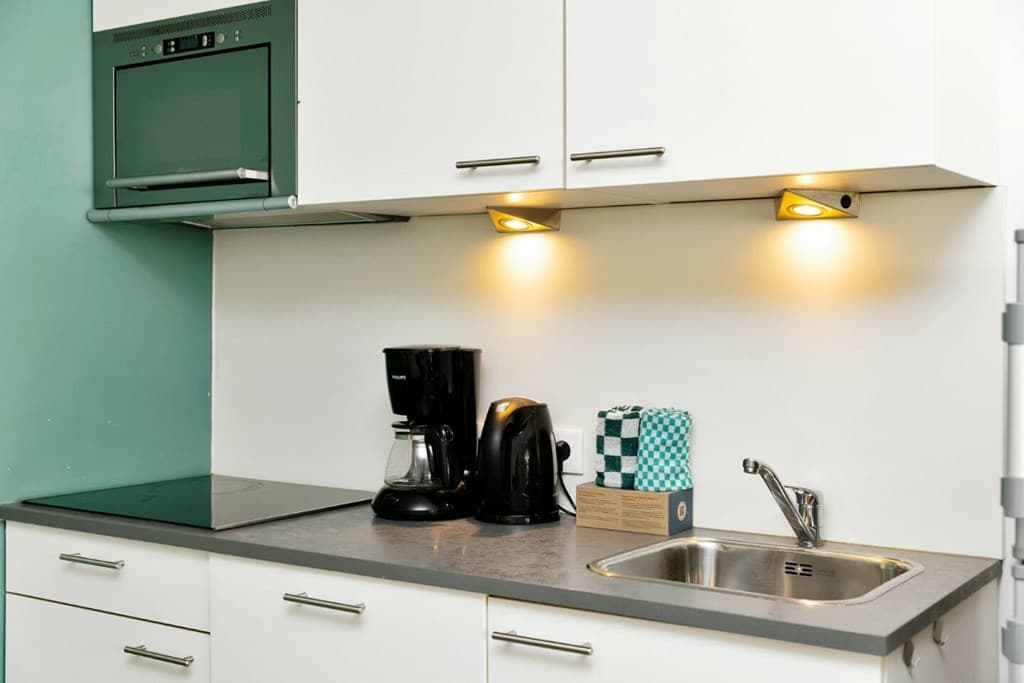 Moderne keuken met kookplaat, koffiezetapparaat, waterkoker en spoelbak, subtiele verlichting boven het aanrecht.