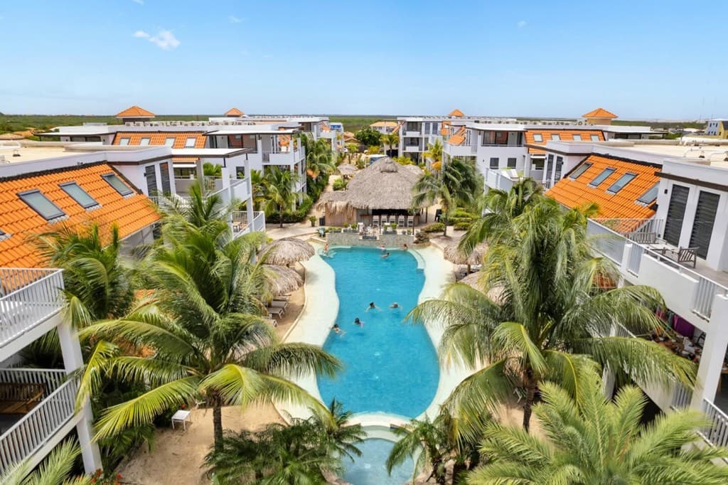 Uitzicht op het zwembad omringd door palmbomen en appartementen met oranje daken in Delfins Beach Resort Bonaire