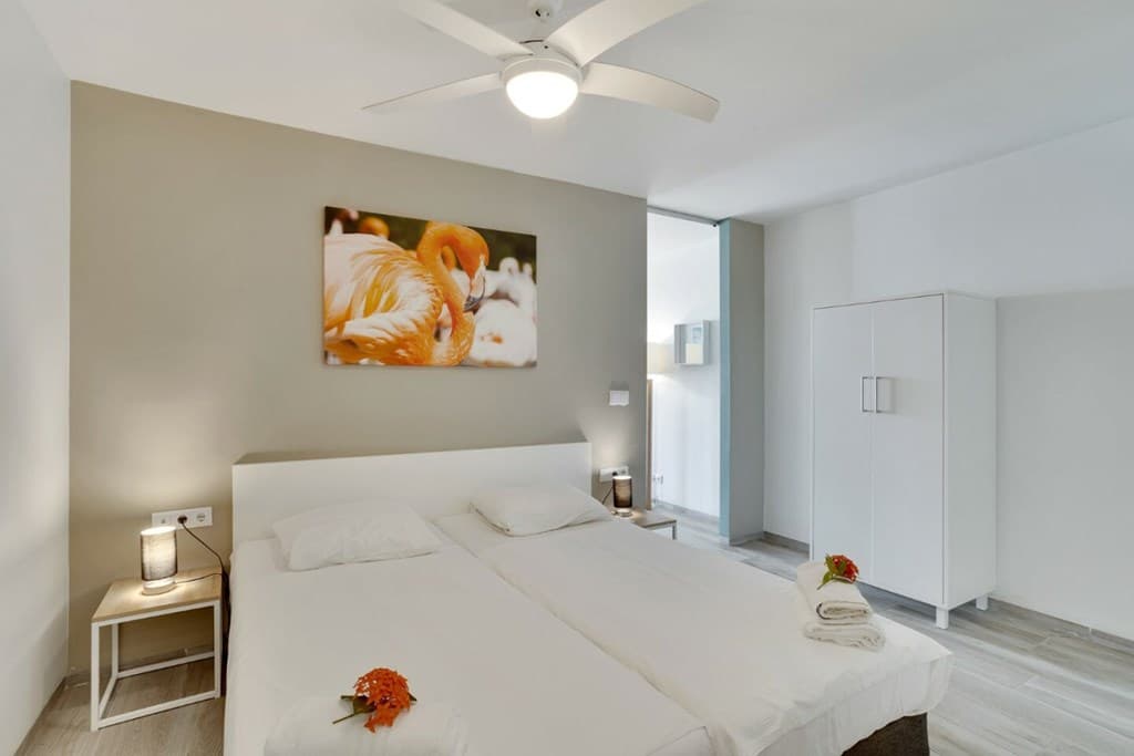 Slaapkamer met twee eenpersoonsbedden, nachtkastjes, wanddecoratie en een kast in lichte kleuren