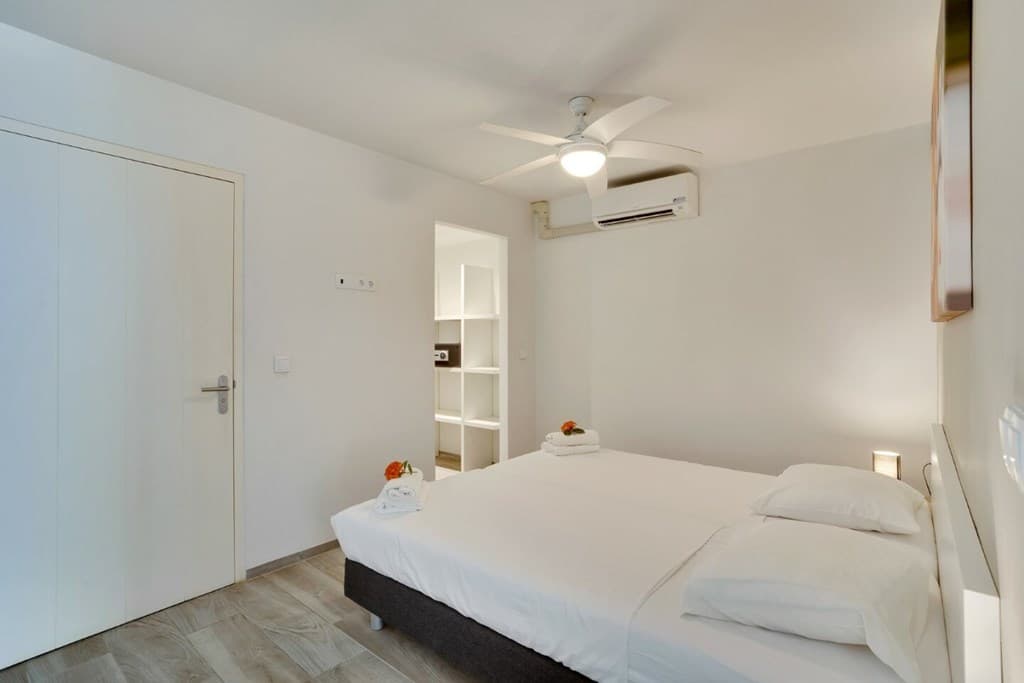 Slaapkamer met twee eenpersoonsbedden, plafondventilator en airco, kast met opbergruimte aan de achterkant van de ruimte