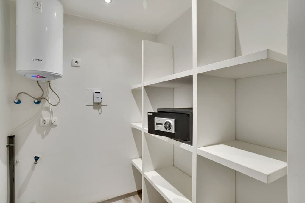Witte inbouwkast met planken, een kluis en een boiler aan de muur, in een neutrale ruimte.