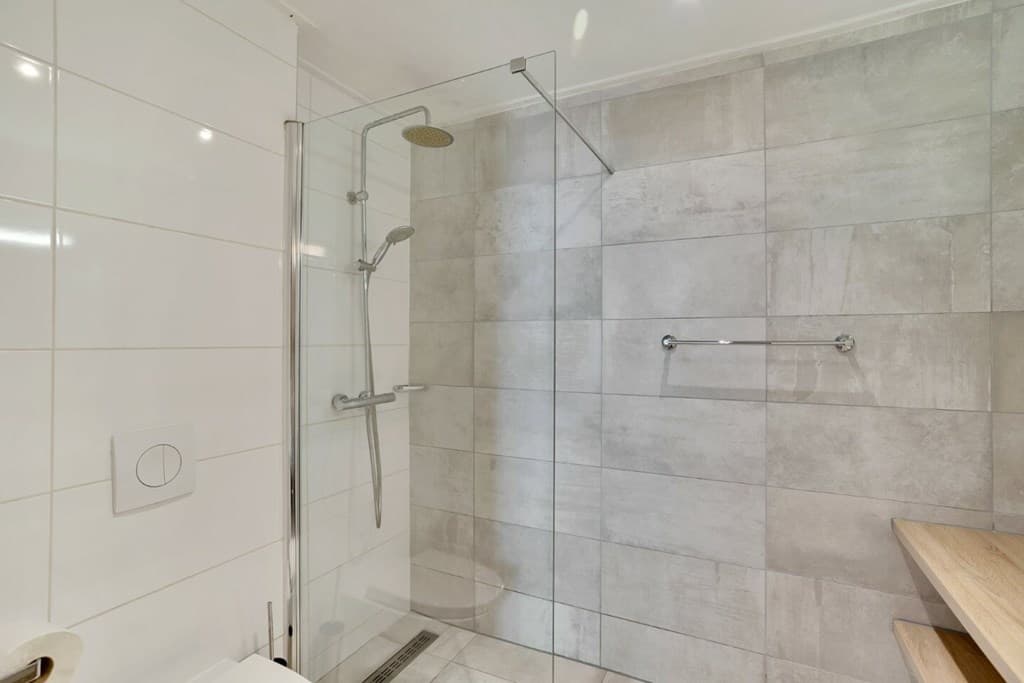 Moderne badkamer met een inloopdouche, grijze tegels en een houten plank aan de muur.