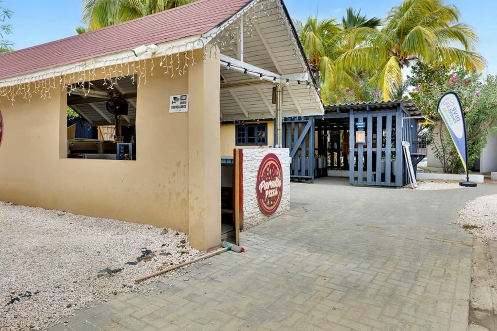 Toegang tot het restaurant met overdekt terras, omringd door palmbomen en grindpaden, bij Delfins Beach Resort.