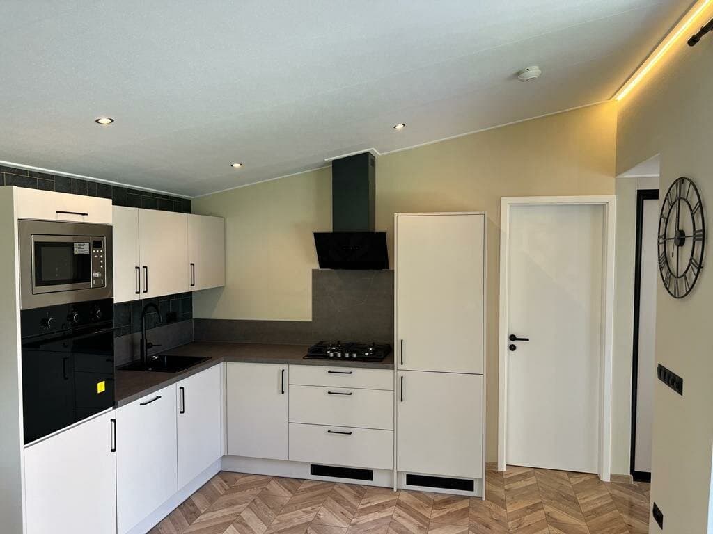 Moderne keuken met zwarte en witte kasten, inbouwapparatuur en een lichte tegelwand, met een houten vloer en natuurlijk licht