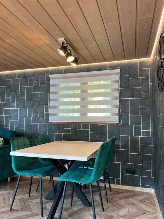 Eetruimte met een moderne tafel en vier groene stoelen, verlicht door spotjes en met een decoratieve wandafwerking.