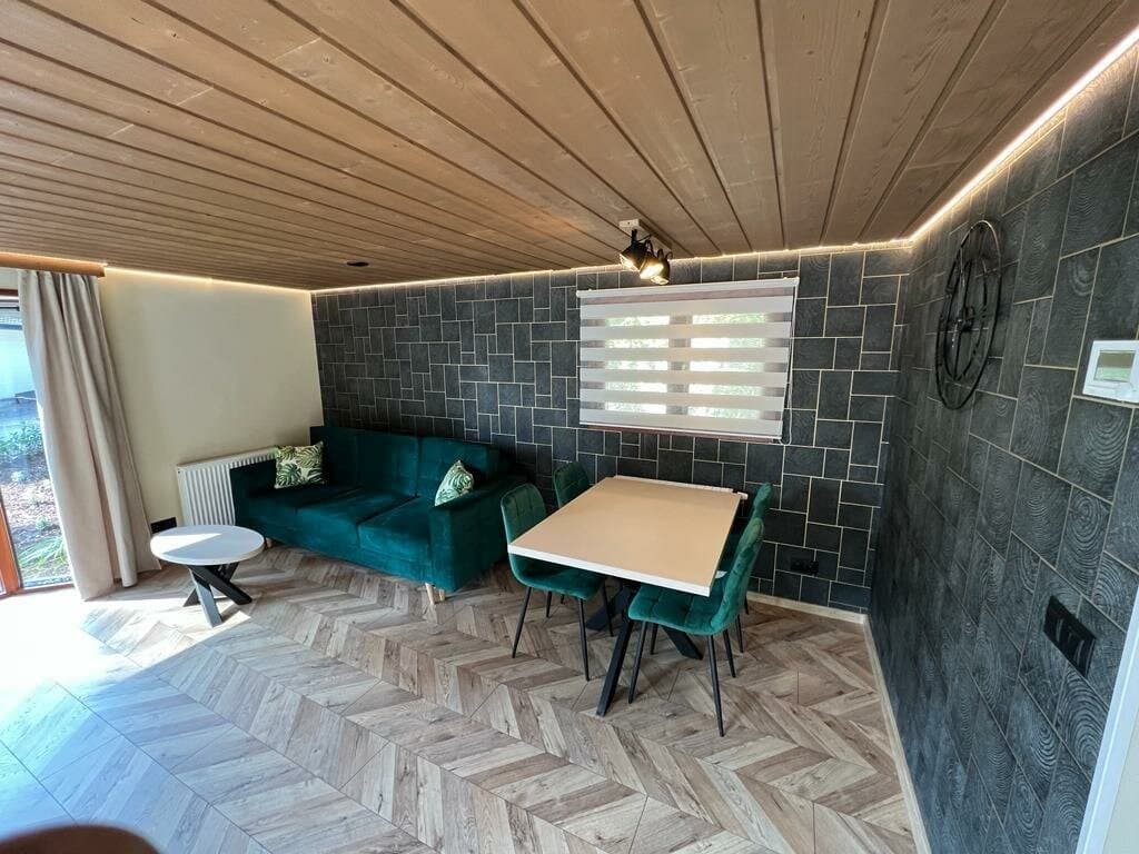 Interieur van een woning met een groene bank, eettafel en houten plafond, evenals een stenen muur en laminaatvloer