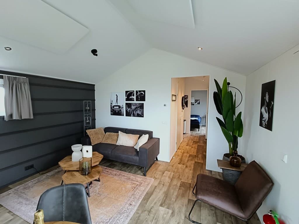 Woonkamer met grijze wand, bank, fauteuils, salontafel en kunst aan de muur, met zicht op een gang en andere kamer.