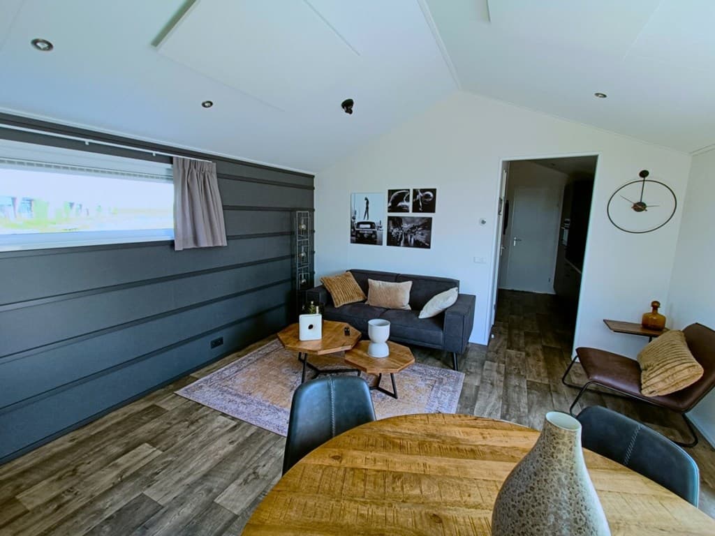Gezellige woonkamer met een bank, houten tafel, decoratieve elementen en uitzicht op de buitenruimte.