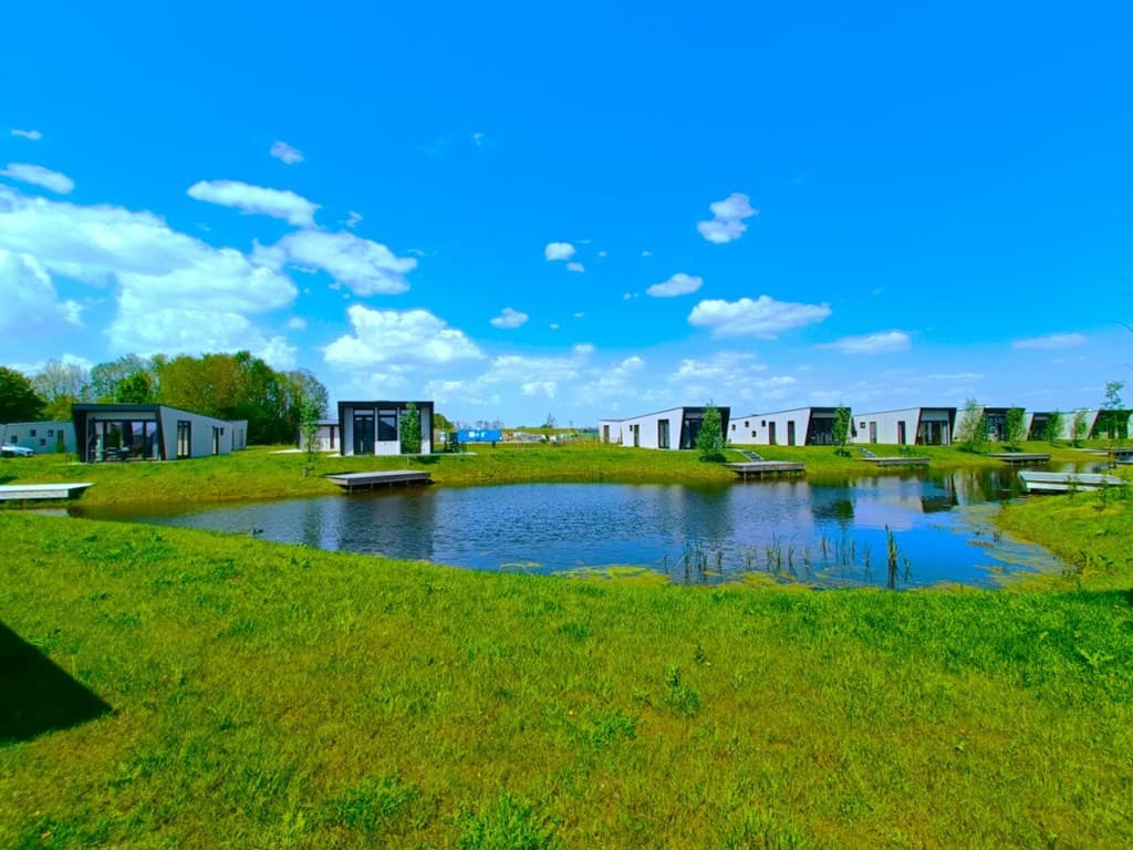 Vakantiewoningen rondom een waterpartij met groene grasvelden en een blauwe lucht met enkele wolken