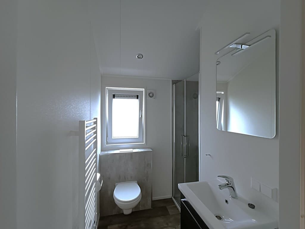 Moderne badkamer met douche, wastafel, toilet en raam voor natuurlijk licht.