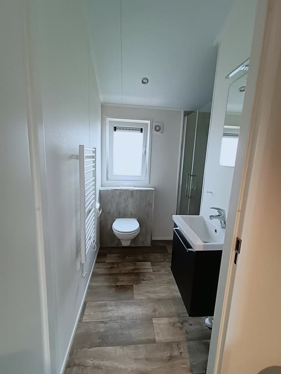 Moderne badkamer met toilet, wastafel en douche, wit en grijs interieur met houten vloer en raam voor natuurlijk licht