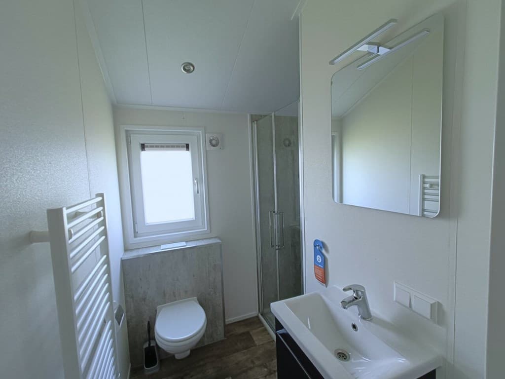 Moderne badkamer met toilet, douche, wastafel en een spiegel, verlicht door natuurlijk licht vanuit het raam.