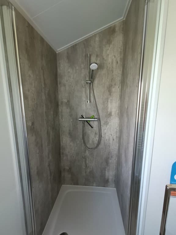 Doucheruimte met moderne inrichting en grijze wandbekleding, voorzien van een doucheset en douchebak.