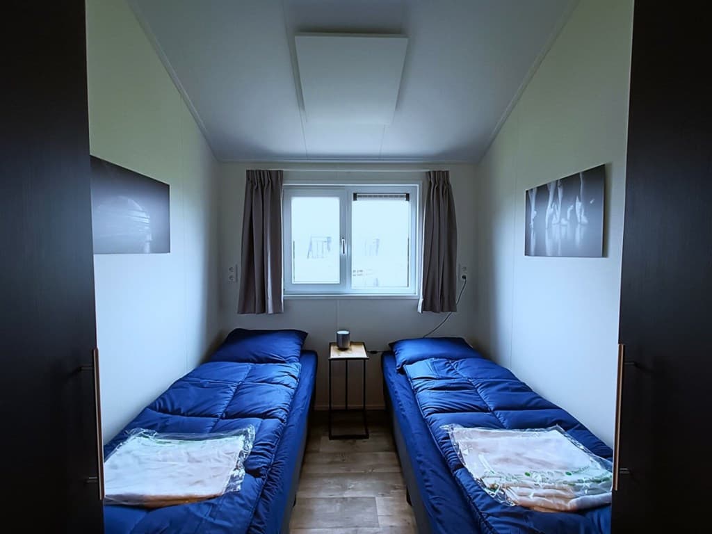 Slaapkamer met twee aparte bedden, een nachttafeltje en een raam met gordijnen