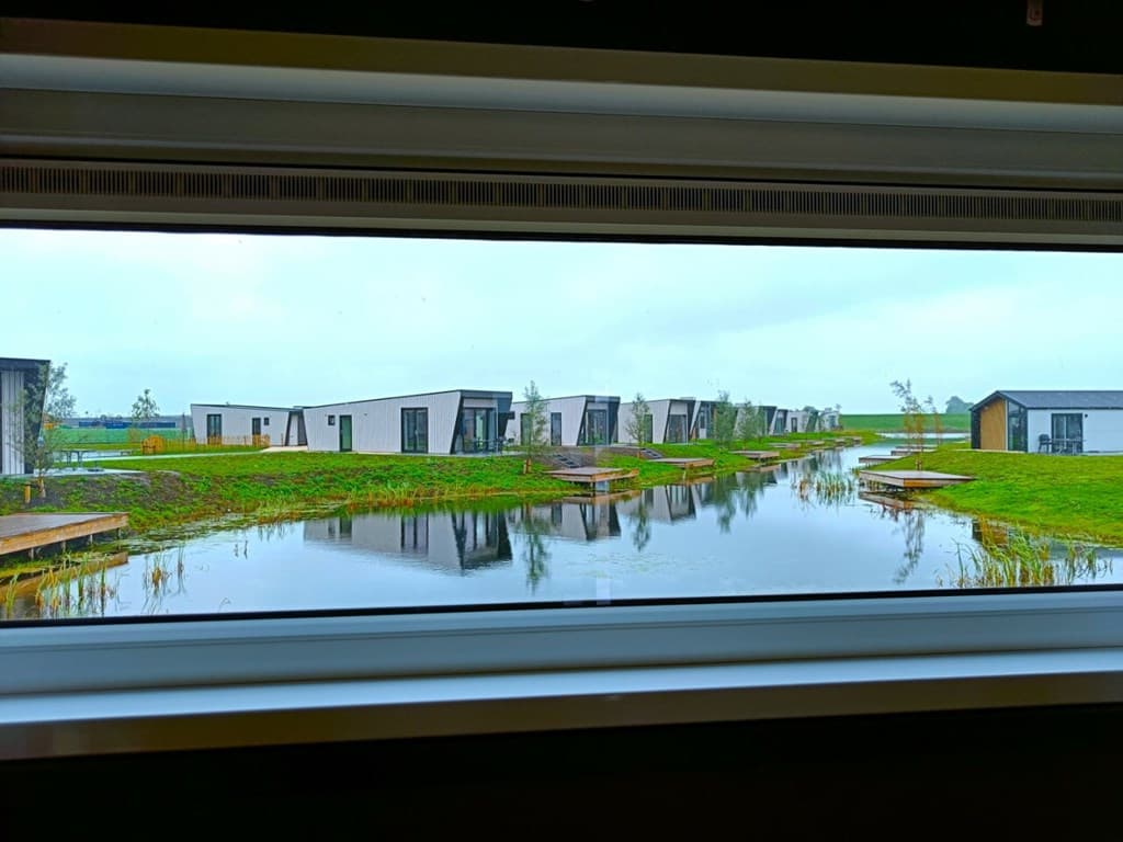 Uitzicht vanuit een raam op EuroParcs De IJssel Eilanden met vakantiewoningen rond een waterpartij en groene omgevingen.